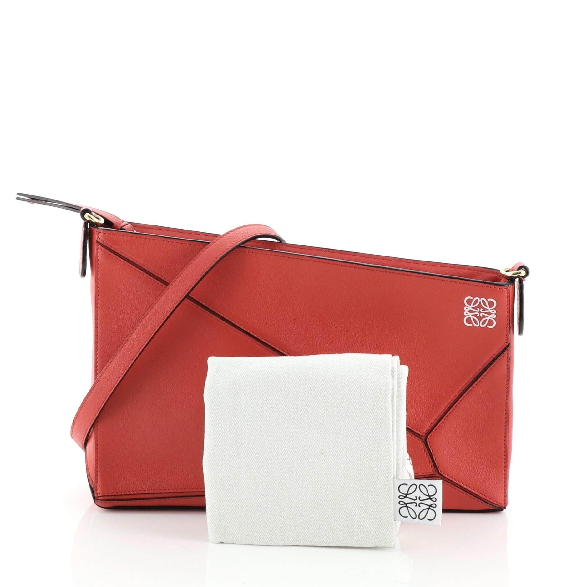 This Loewe Puzzle Pochette Bag Leather Mini, crafted in red leather, features detachable strap, exterior zip pocket and gold-tone hardware. Its top zip closure opens to a black fabric interior with slip pockets. 

Estimated Retail Price: