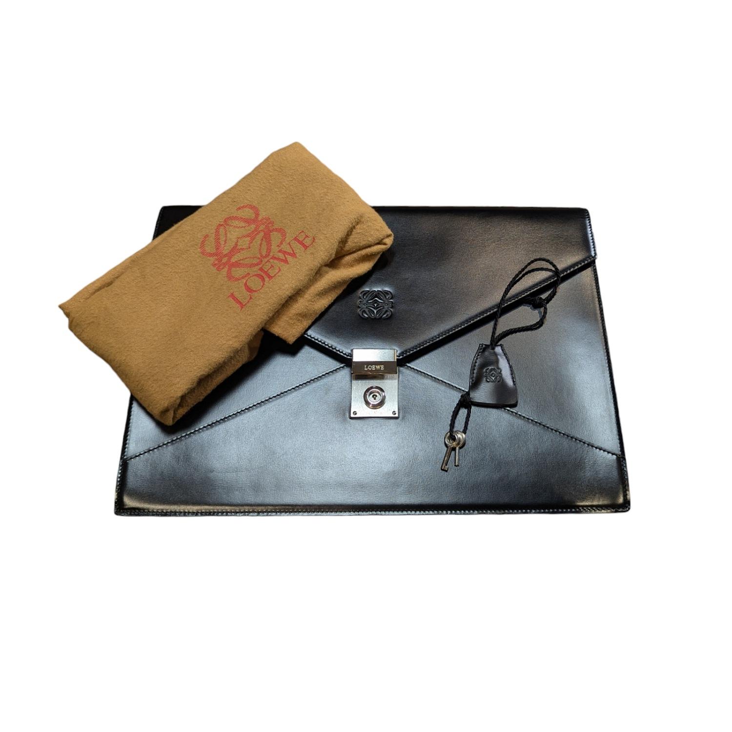 This Vintage Loewe Envelope-style Portfolio is crafted of genuine Black Leather with Silver-Tone Hardware. It features a Push-Lock Closure that opens to a Suede interior Lining. Includes a Clochette, keys and dust bag. NOTE: Only 1 key is functional