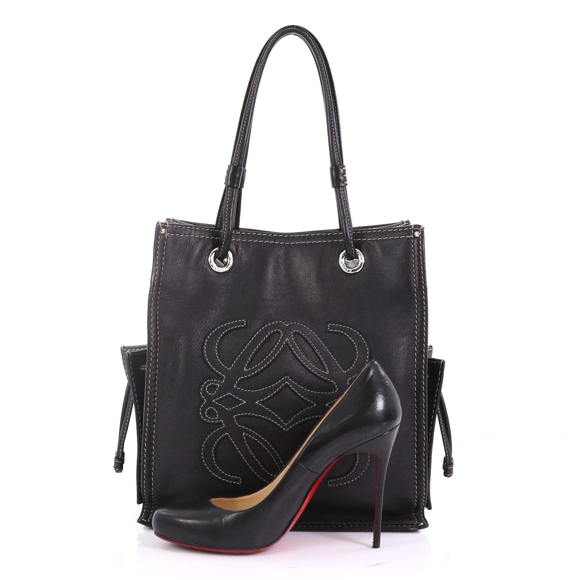 This Loewe Vintage Logo Tote Leather Medium, crafted from black leather, features dual leather straps, standout contrast stitching, exterior side pocket with cinch closure, and silver-tone hardware. Its magnetic snap closure opens to a black fabric