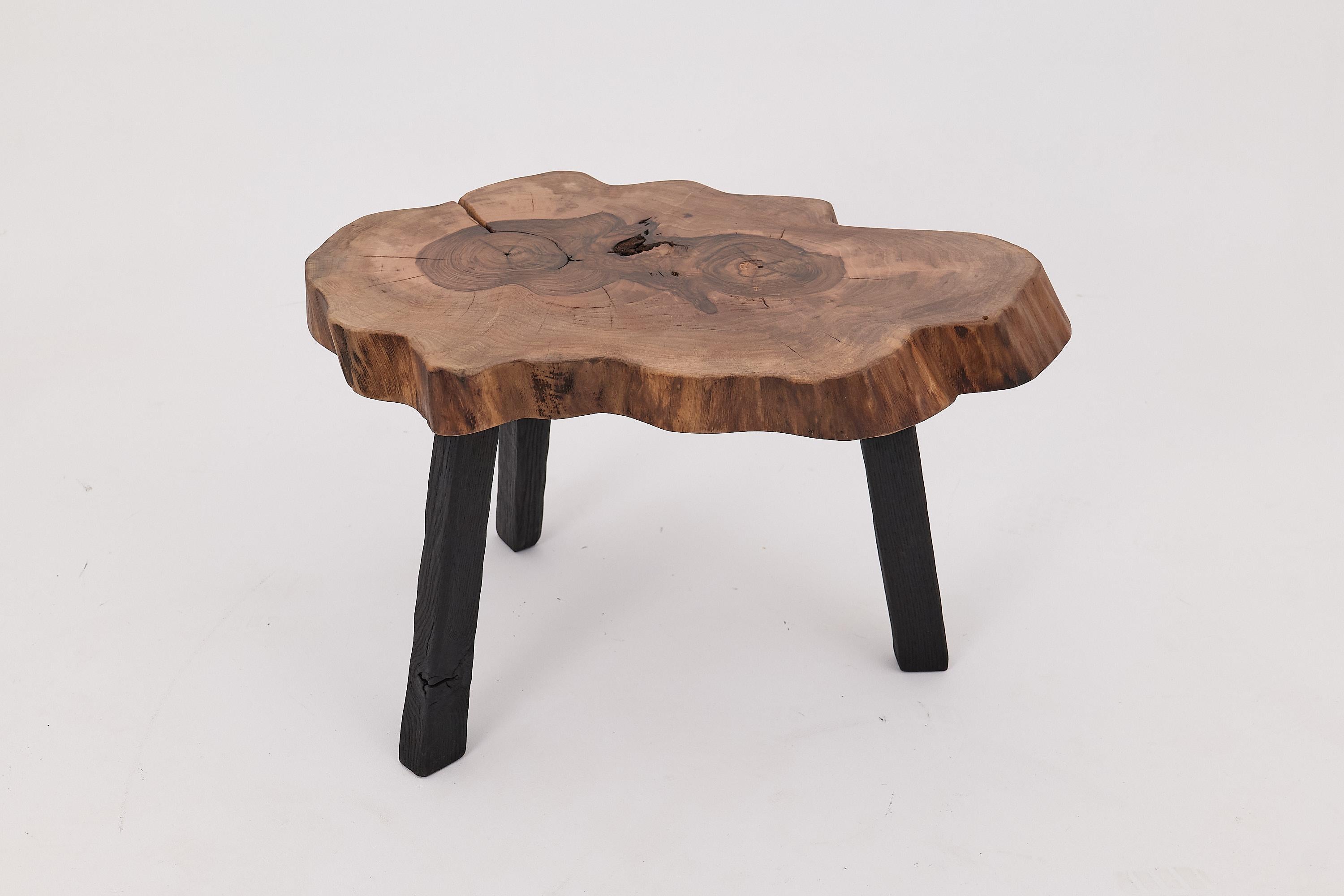 Cette table d'appoint à bord organique est une célébration de l'élégance indisciplinée de la nature, fabriquée à la main à partir d'une seule plaque de bois dur massif. Le plateau de table conserve sa silhouette brute et libre - façonnée par la