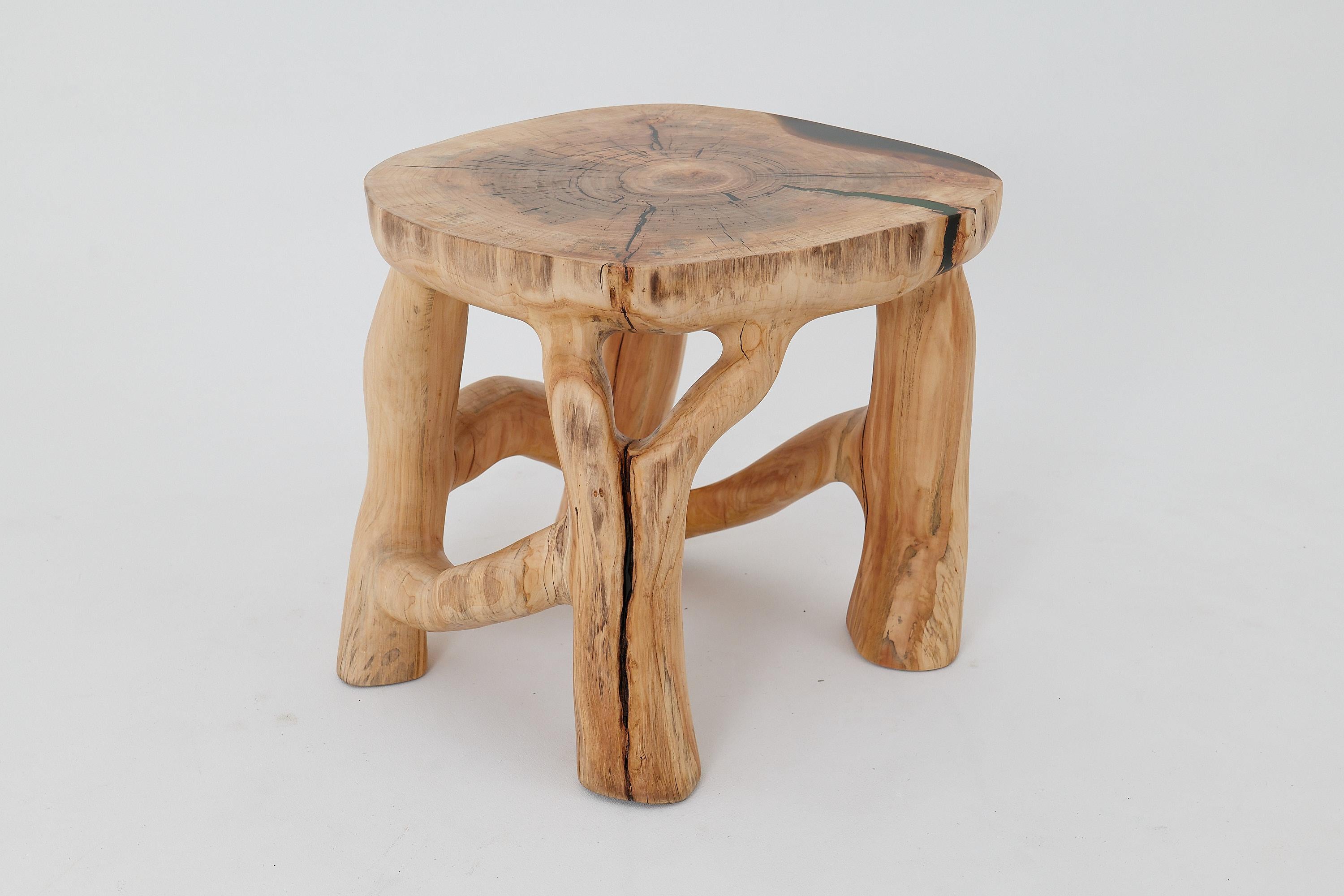 This sculptural side table is a one-of-a-kind piece, carved entirely from a single solid hardwood log. Its design merges organic growth with functional form, as four branch-like legs rise and interconnect to support a broad top that preserves the