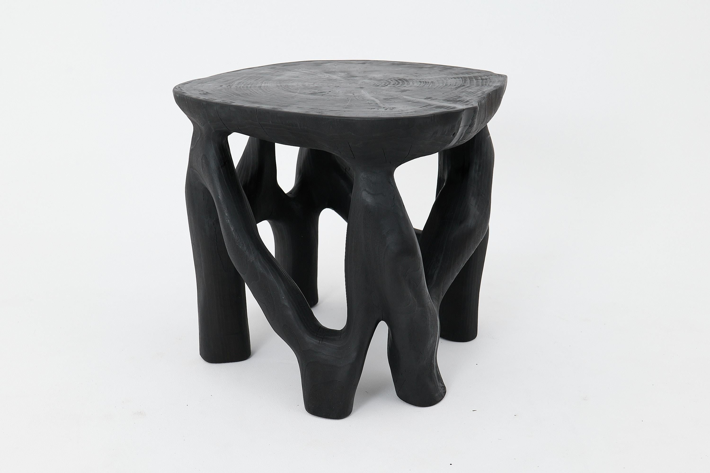 This sculptural side table is a one-of-a-kind creation, hand-carved from a single solid hardwood log and finished in deep black through the traditional shou sugi ban charring technique. Its branching legs twist and merge in an organic rhythm,