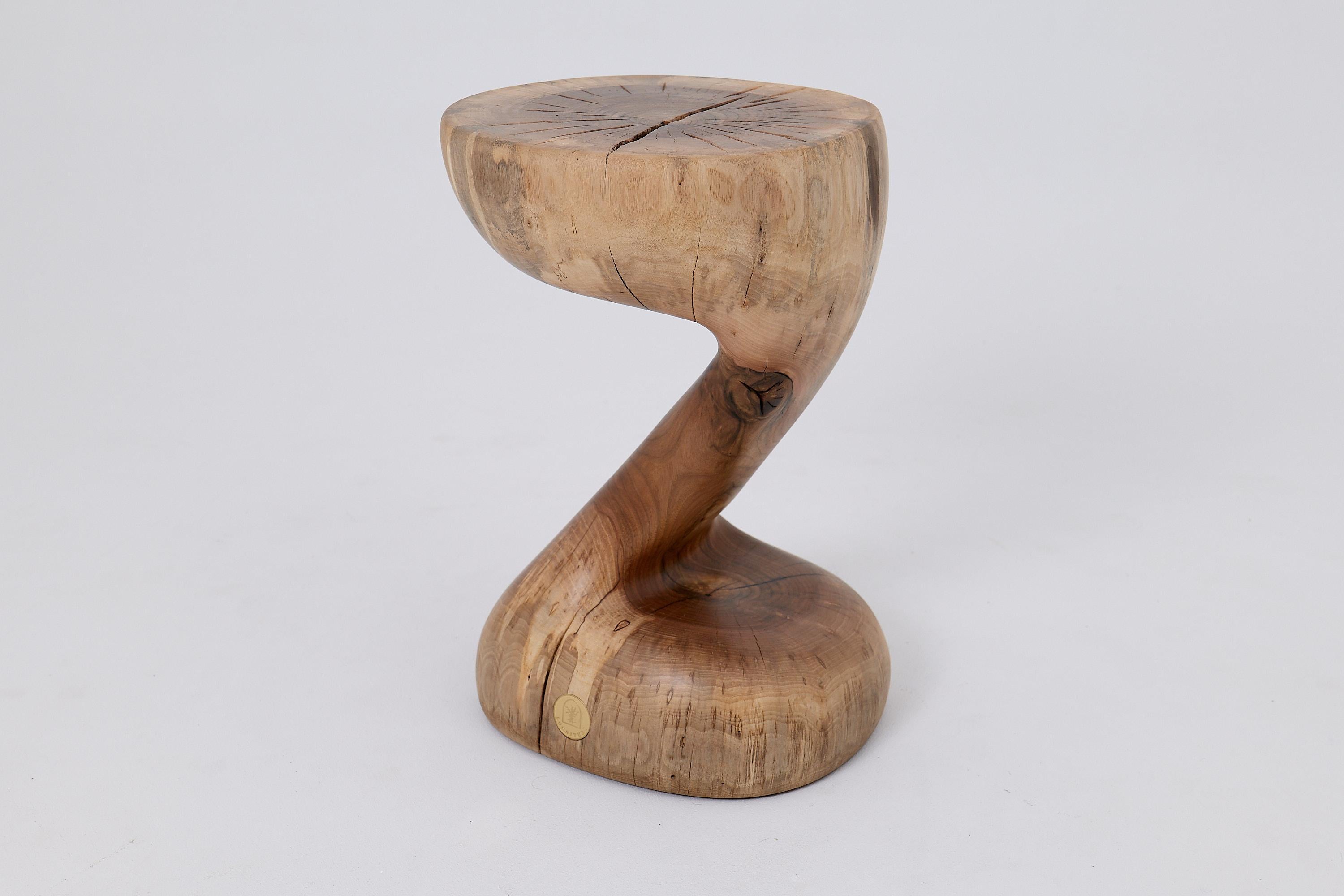 This extraordinary sculptural side table is a one of a kind piece, carved entirely by hand from a single solid hardwood log. Its captivating form is defined by an elegant, continuous swirl, a dynamic twist that makes the heavy timber appear to defy