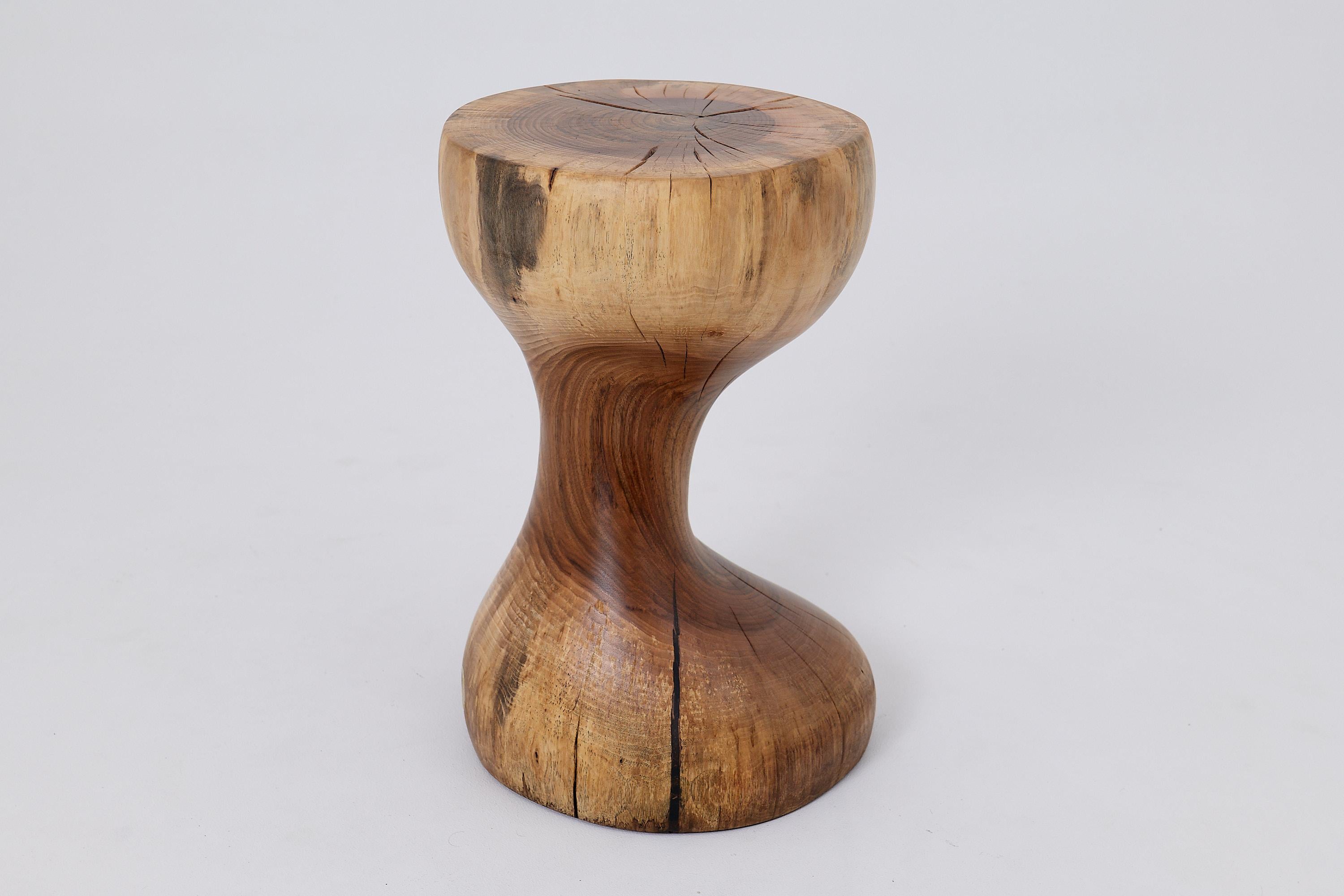 This biomorphic side table is a singular work of art, hand carved from a single hardwood log to achieve a perfect hourglass silhouette. Its form is a study in fluid curves and organic balance, creating a sense of graceful movement frozen in time.