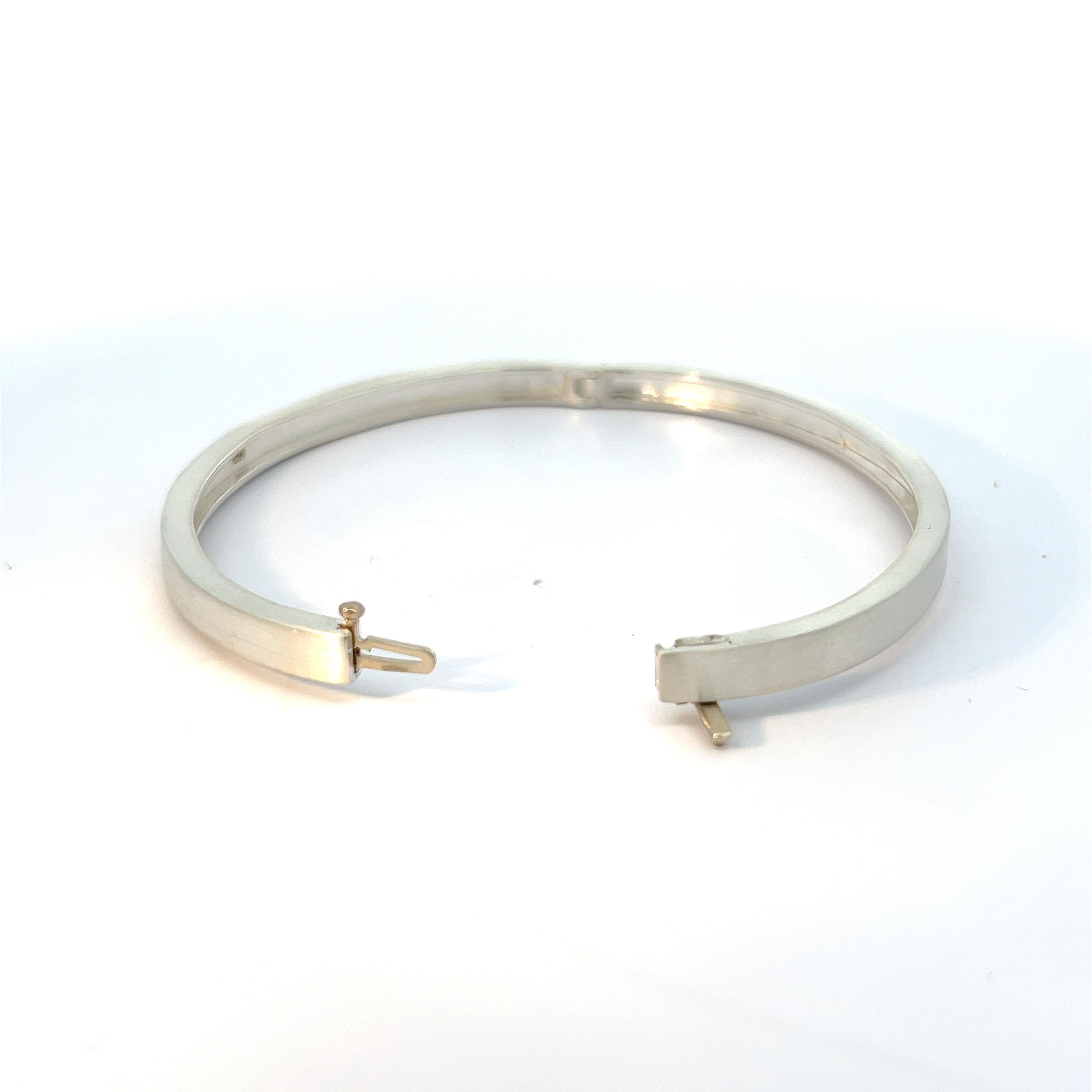 Indulge in understated luxury with this distinguished men's bangle bracelet, meticulously crafted in gleaming sterling silver. The brushed finish lends a subtle yet sophisticated texture to the surface, adding depth and character to this timeless