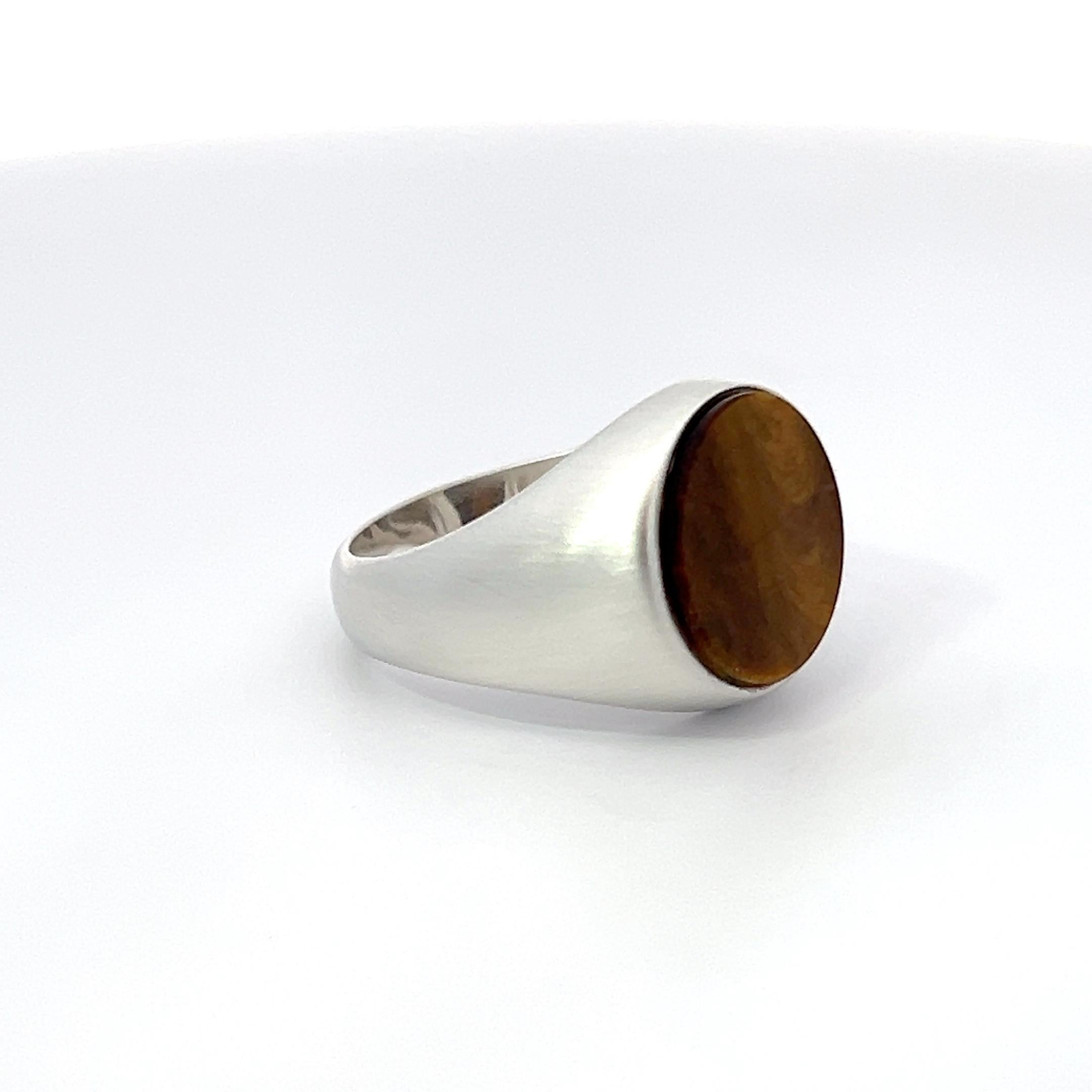 Introducing the Lois D. Sasson Design Sterling Silver Tiger Eye Signet Men's Ring. This exceptional piece features a matte finish sterling silver band that exudes refined elegance. At its center, a stunning round tiger eye stone is set, showcasing