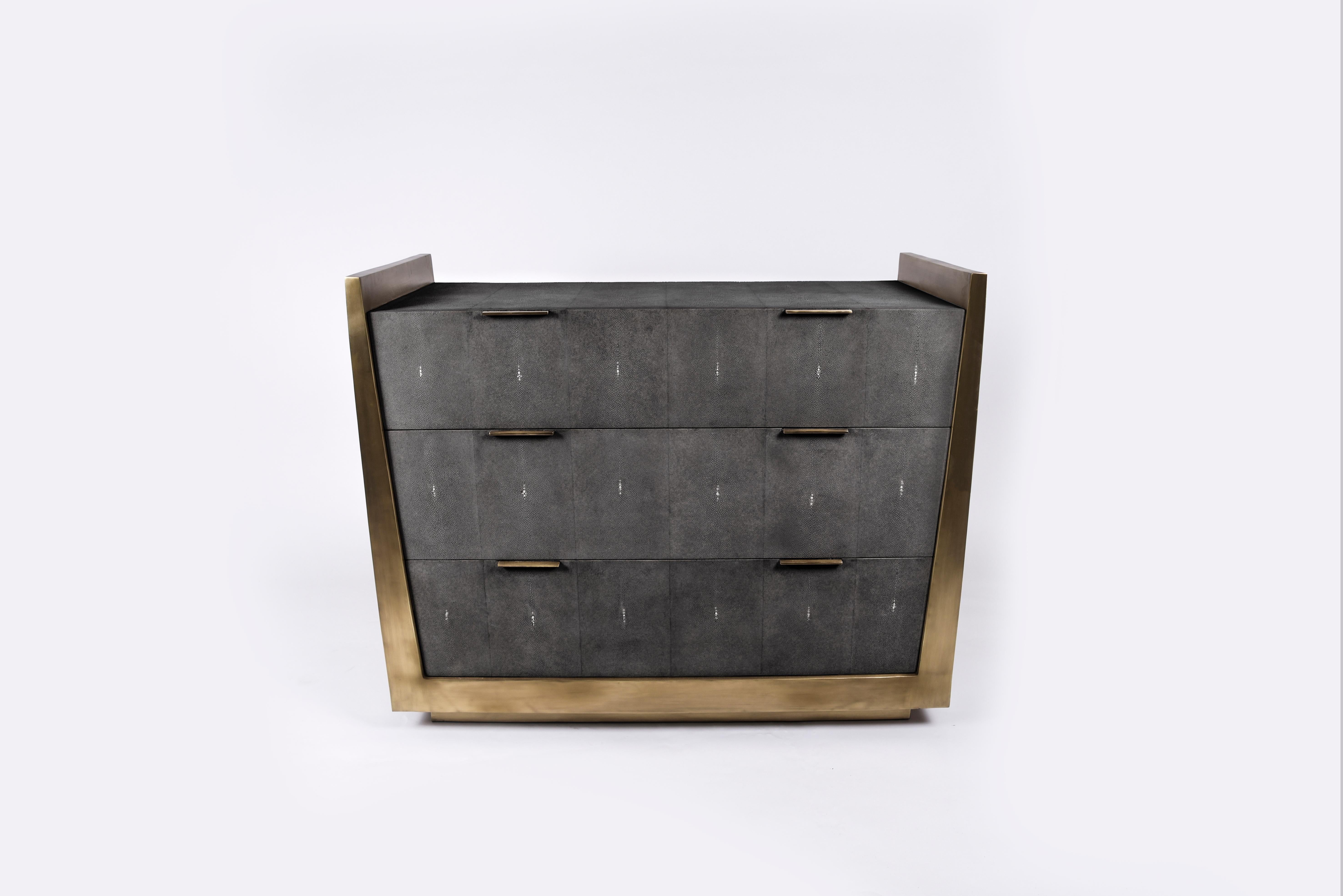 La commode Lola de R&Y Augousti est une pièce élégante à la géométrie subtile. Cette commode est incrustée de galuchat noir de charbon, les côtés étant entièrement incrustés de laiton bronze-patine. La pièce est complétée par de discrètes poignées
