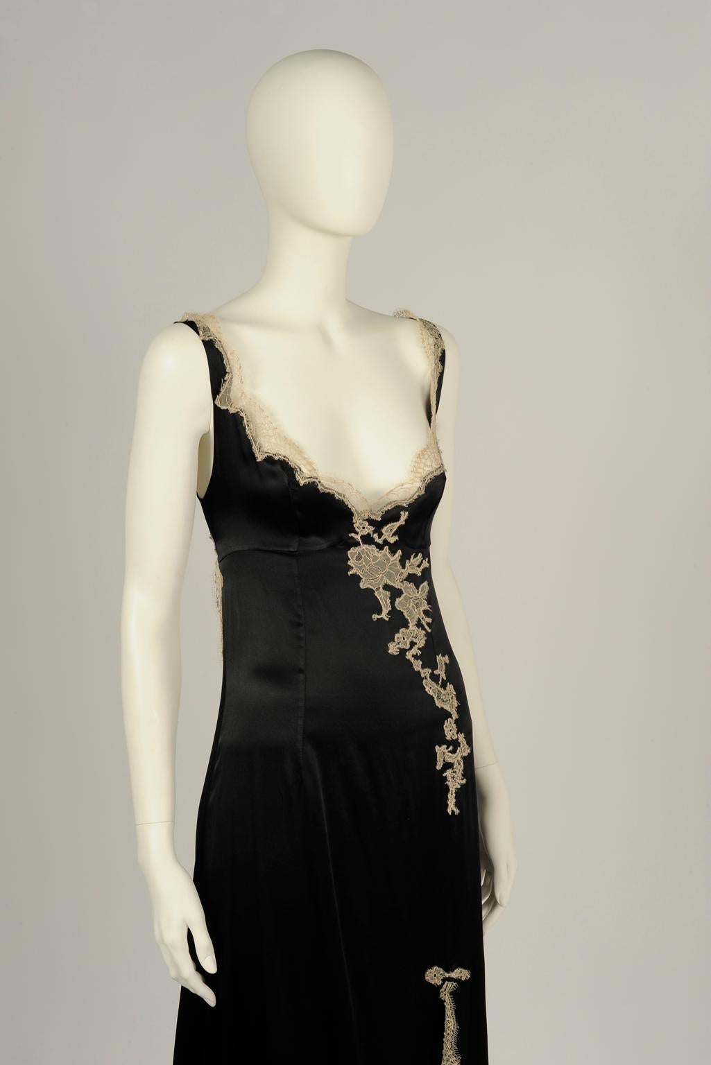 Traced with delicate beige Calais lace, this stunning runway gown is cut from black silk-satin. Unbelievably sexy side front slit and cutout back. Unlined, the slip dress fastens with a concealed zip and a small black button at the back (see