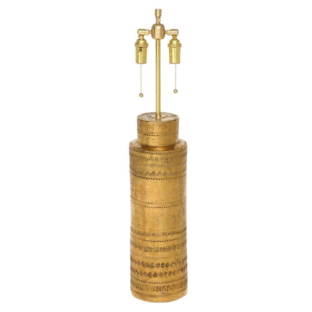 Aldo Londi Bitossi Table Lamp, Metallic Gold Ceramic, Signed. Tall cylinder body with stepped neck in gold metallic glaze. Decorated with bands of embossed patterns. Signed on underside. Measure: Ceramic only is 22.5 inches. Measure to the bottom of