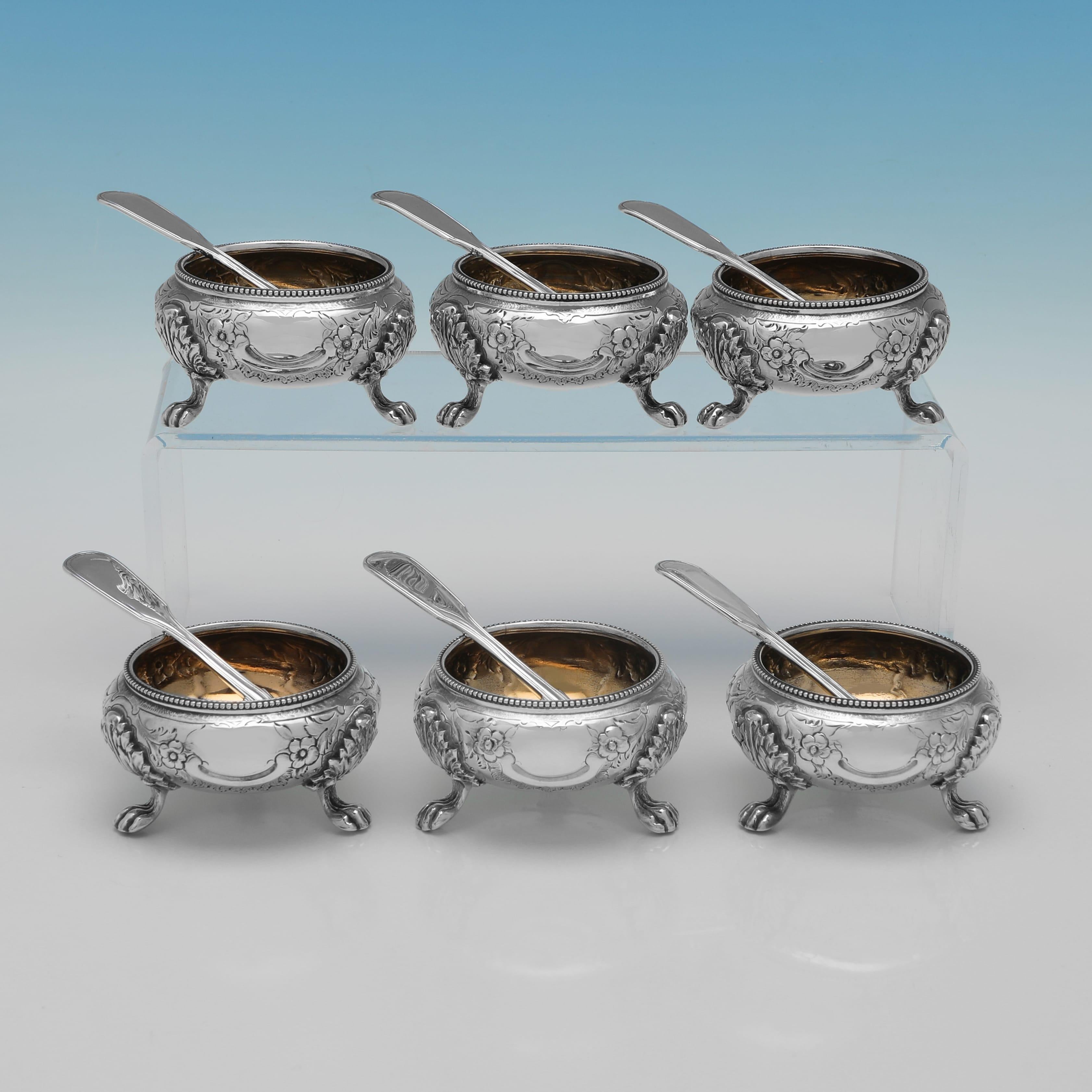 Poinçonné à Londres en 1880 par Goldsmiths Alliance Ltd, cet ensemble de six salières et six cuillères en argent sterling ancien et orné présente des bols circulaires doublés de dorure avec un décor de feuillage en relief et des bordures perlées