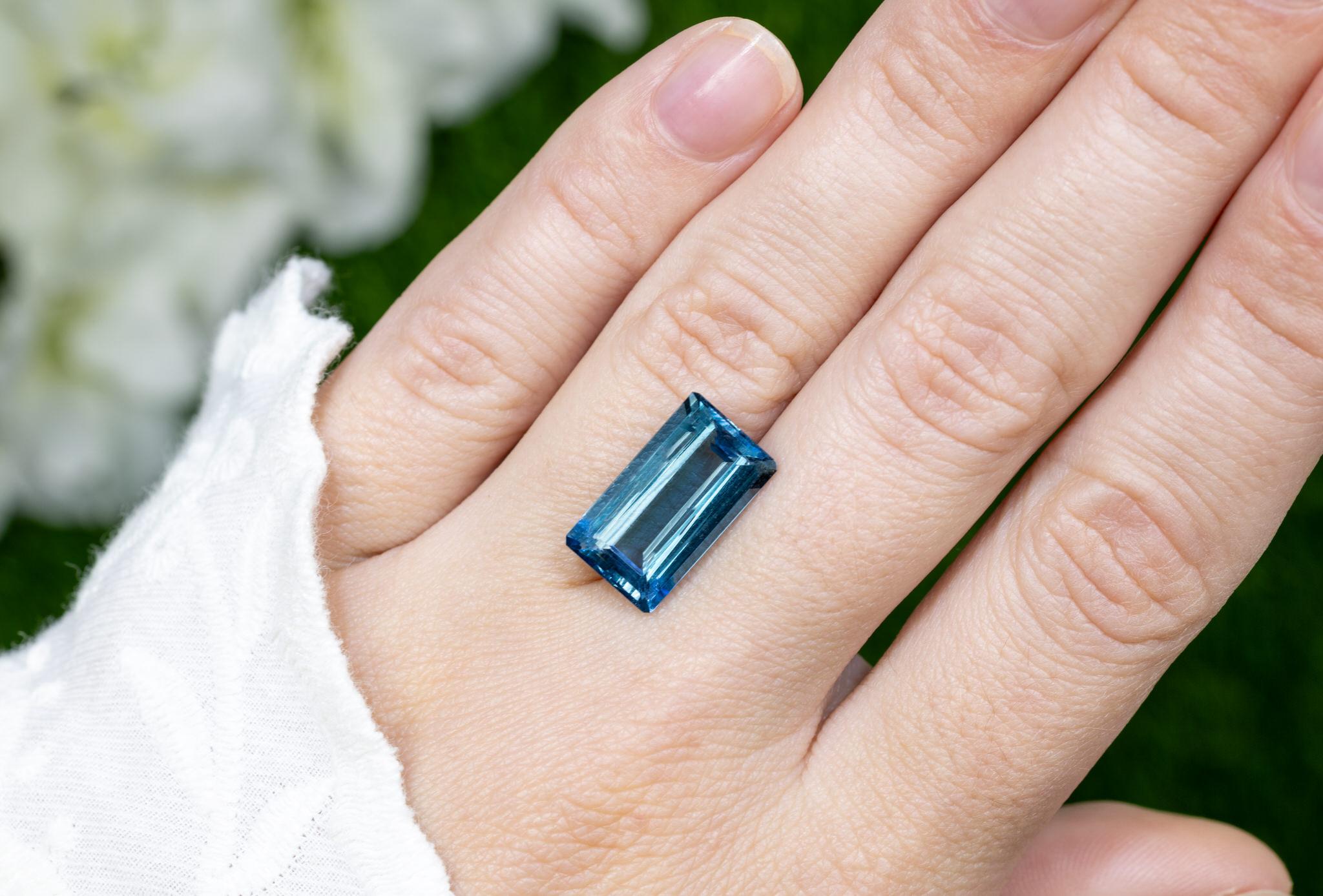 This 7.90 carat London Blue Topaz captivates with its deep teal-blue color, reminiscent of the mysterious depths of the ocean. Precision-cut in a classic emerald cut, this gemstone features elegant step-cut facets that enhance its rich saturation