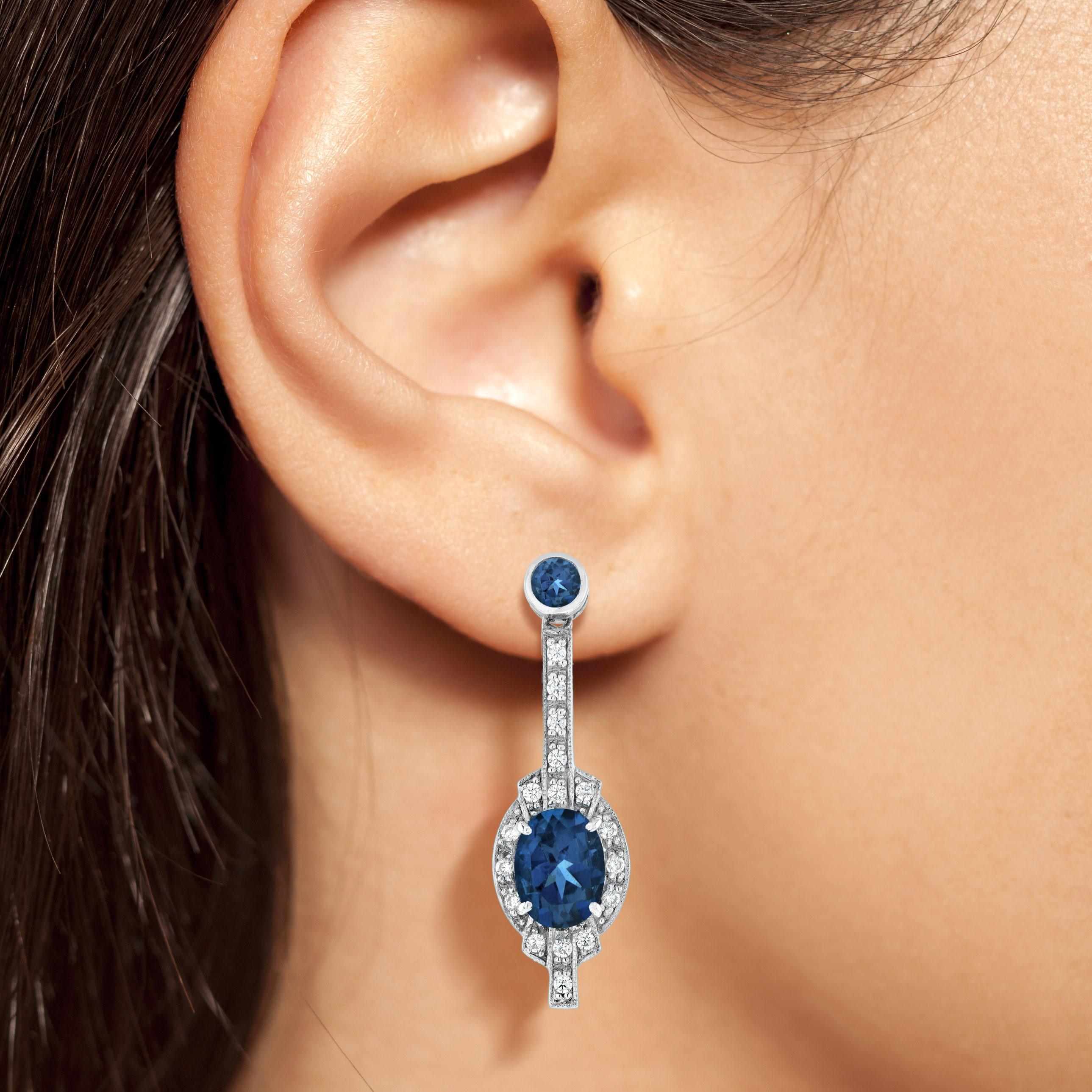 These elegant and incredible 18k white gold Art Deco style earrings feature an oval cut London blue topaz, each totaling approximately 3.20 carat in weight, measuring 8 mm. x 6 mm. Both topaz are intensely saturated with that deep blue color. Each