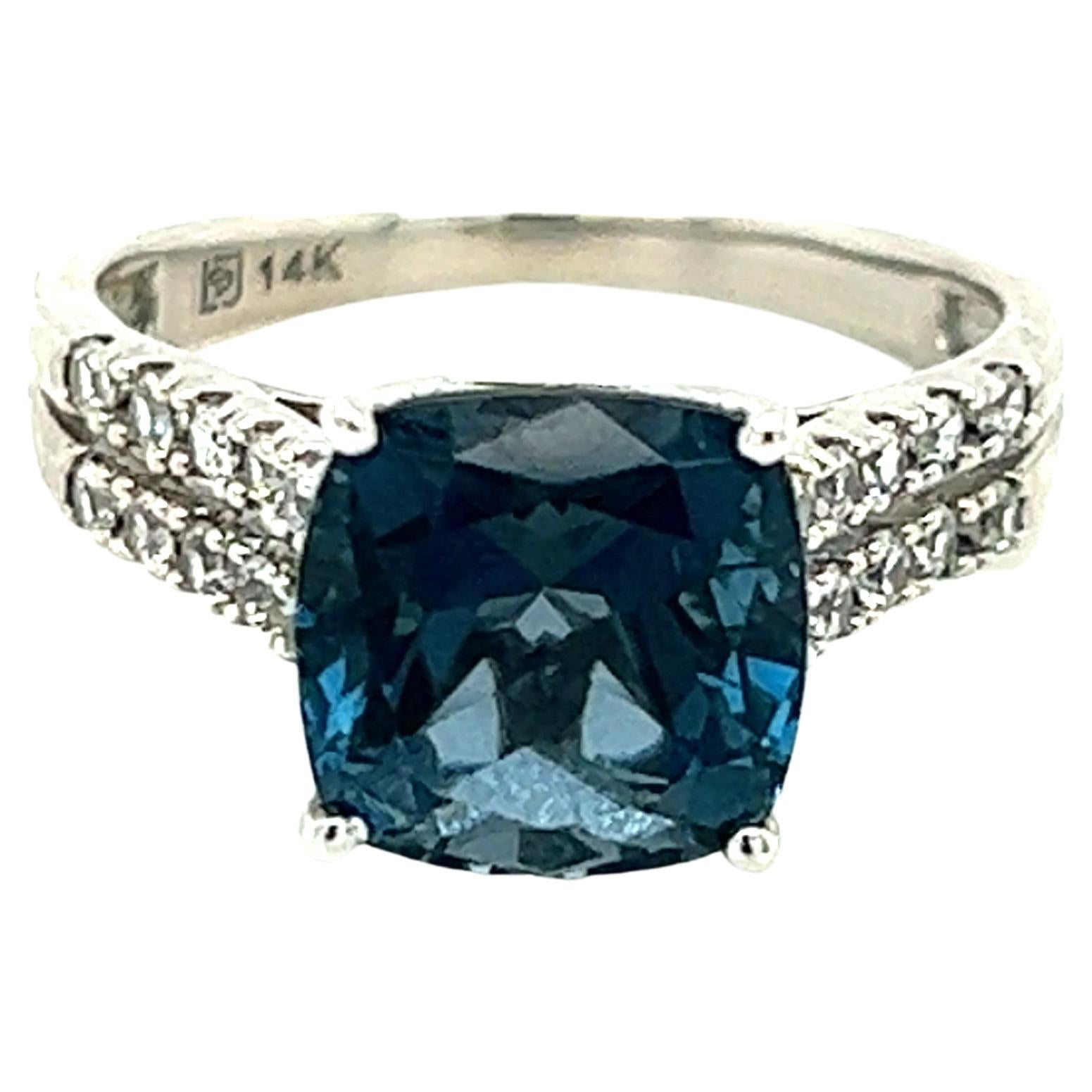 Ein Ring aus 14-karätigem Weißgold, besetzt mit einem (1) 9 mm großen Londoner Blautopas im Kissenschliff, flankiert von zwanzig (20) 1,5 mm großen weißen Saphiren im Brillantschliff.  Der Schaft misst am oberen Ende des Rings 3,90 mm und verjüngt