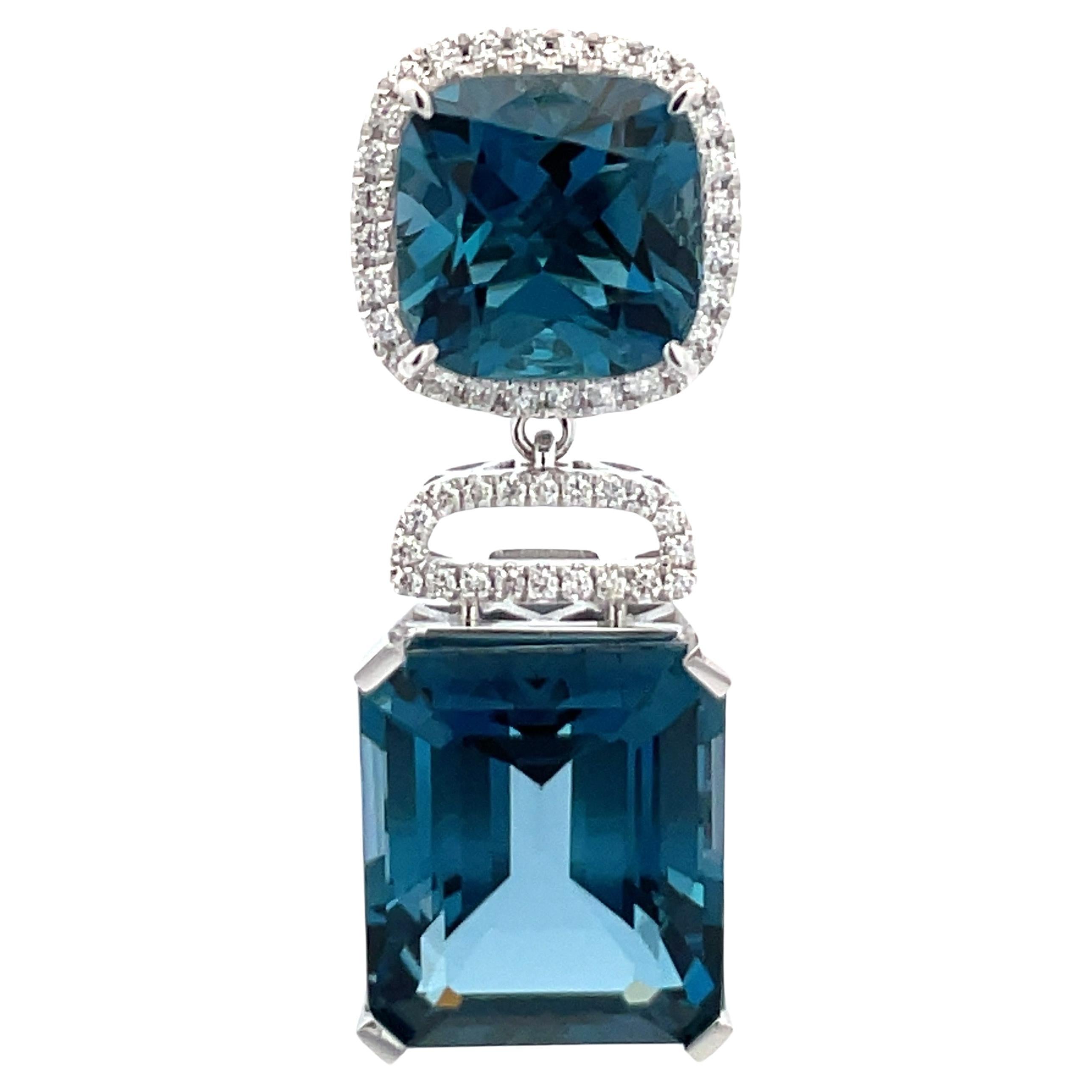 14 Karat White Gold drop earrings featuring two Cushion London Blue Topaz weighing 9.83 Carats, to Emerald Cut weighing 25.34 and a diamond halo containing 96 round brilliants, 0.55 carats.