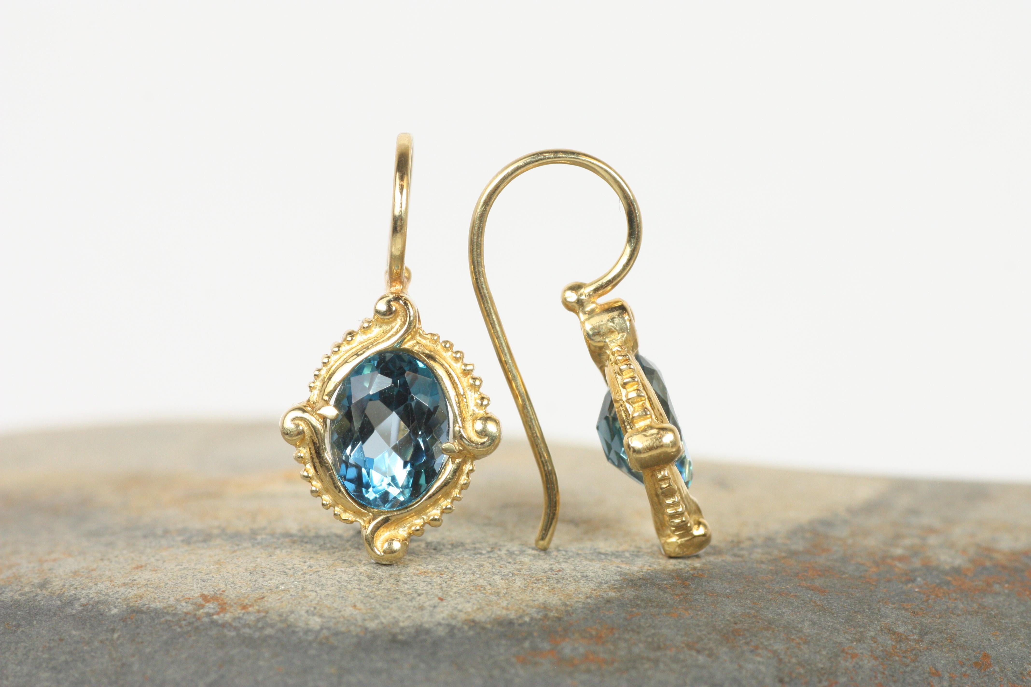 Elevate your look with the Four Winds Earrings, featuring captivating London blue topaz gemstones set in 14K yellow gold. The deep, ocean-like hues of the oval-cut topaz are framed by intricate scrollwork and beaded details, evoking a sense of