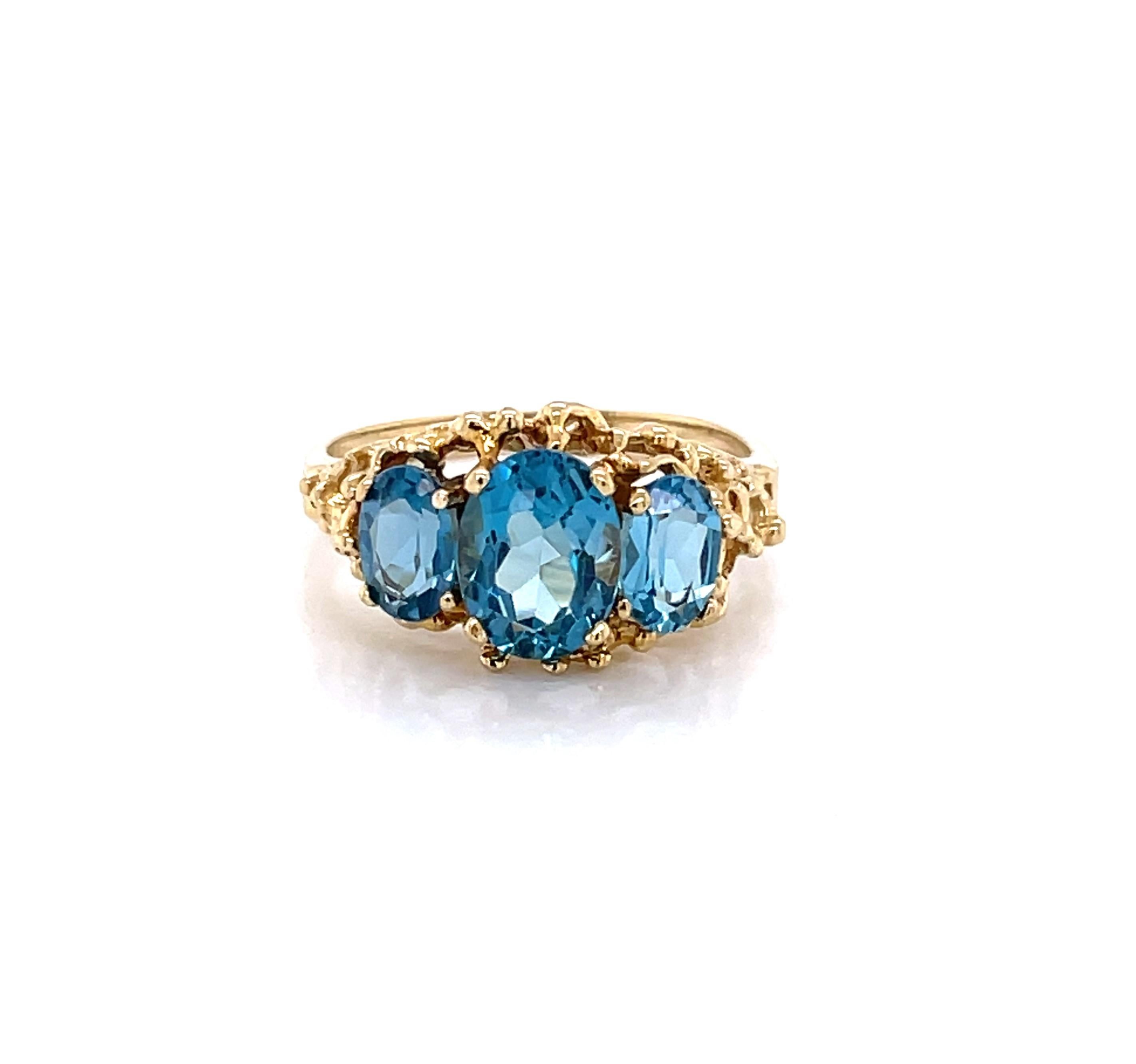 Eye catching London Blue Topaz present vividly set in bright ten karat 10k yellow gold. One 5x8 oval faceted center stone is flank by two matching 3x5 oval stones creating an exciting overall color burst in this vintage style ring setting. In ring