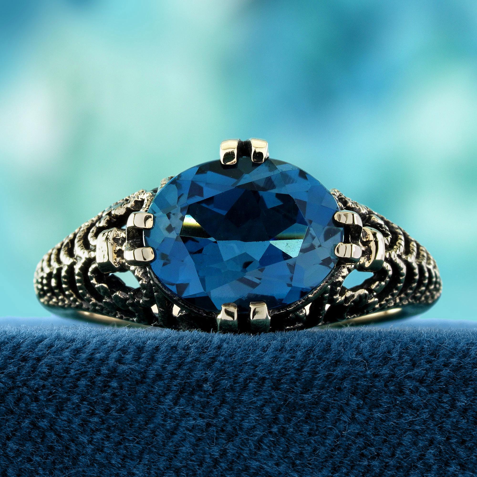 A captivating oval London Blue Topaz sits securely in a classic double prong setting.
The deep, oceanic hue of the stone radiates elegance and depth. Floral filigree details on the shoulders add a romantic, vintage-inspired touch. Expertly crafted
