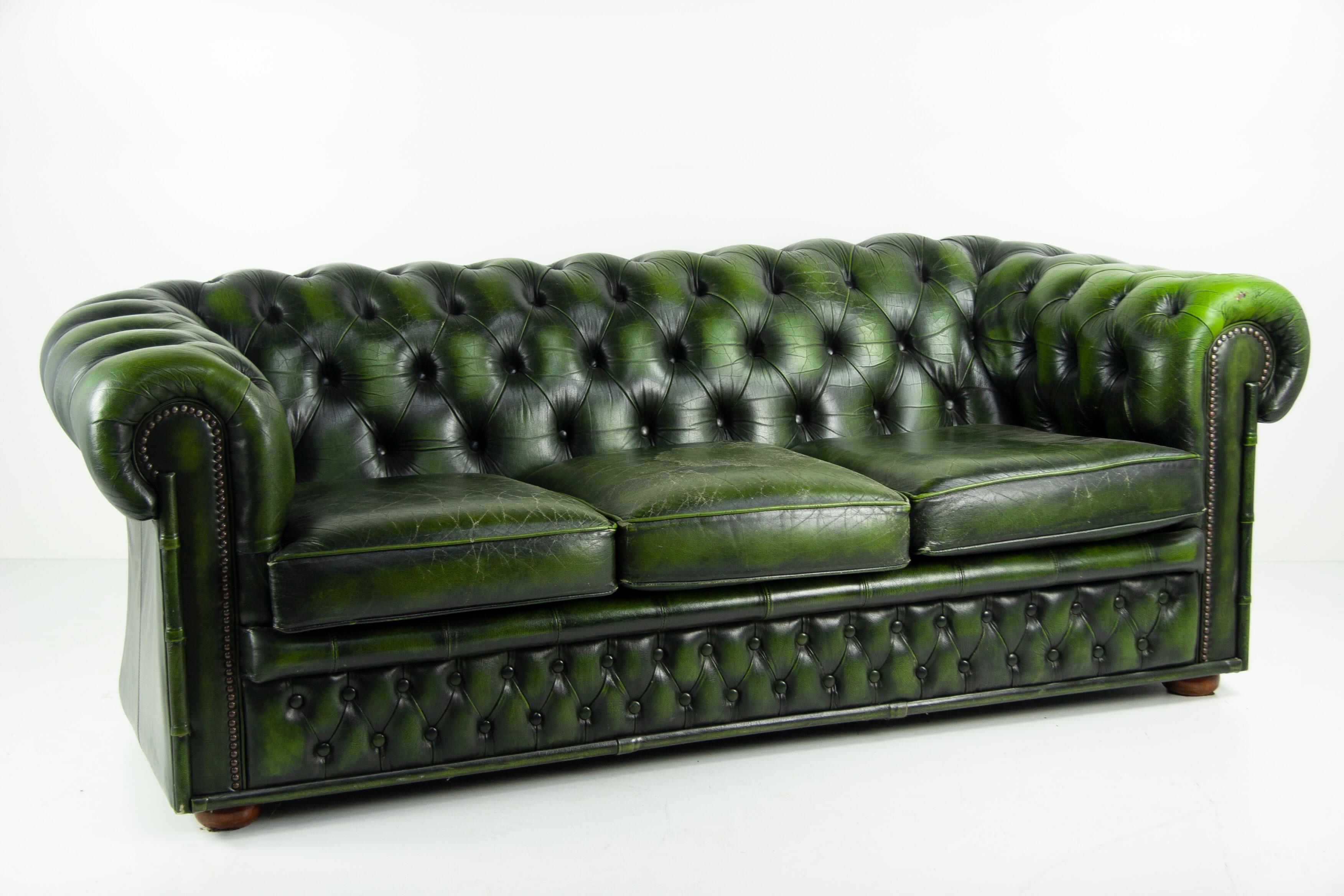 Immerse yourself in the allure of classic British elegance with this Vintage 60s London Chesterfield Sofa. Resplendent in its petrol green leather, this piece is a standout artifact of its era. The rich patina of the leather adds depth and