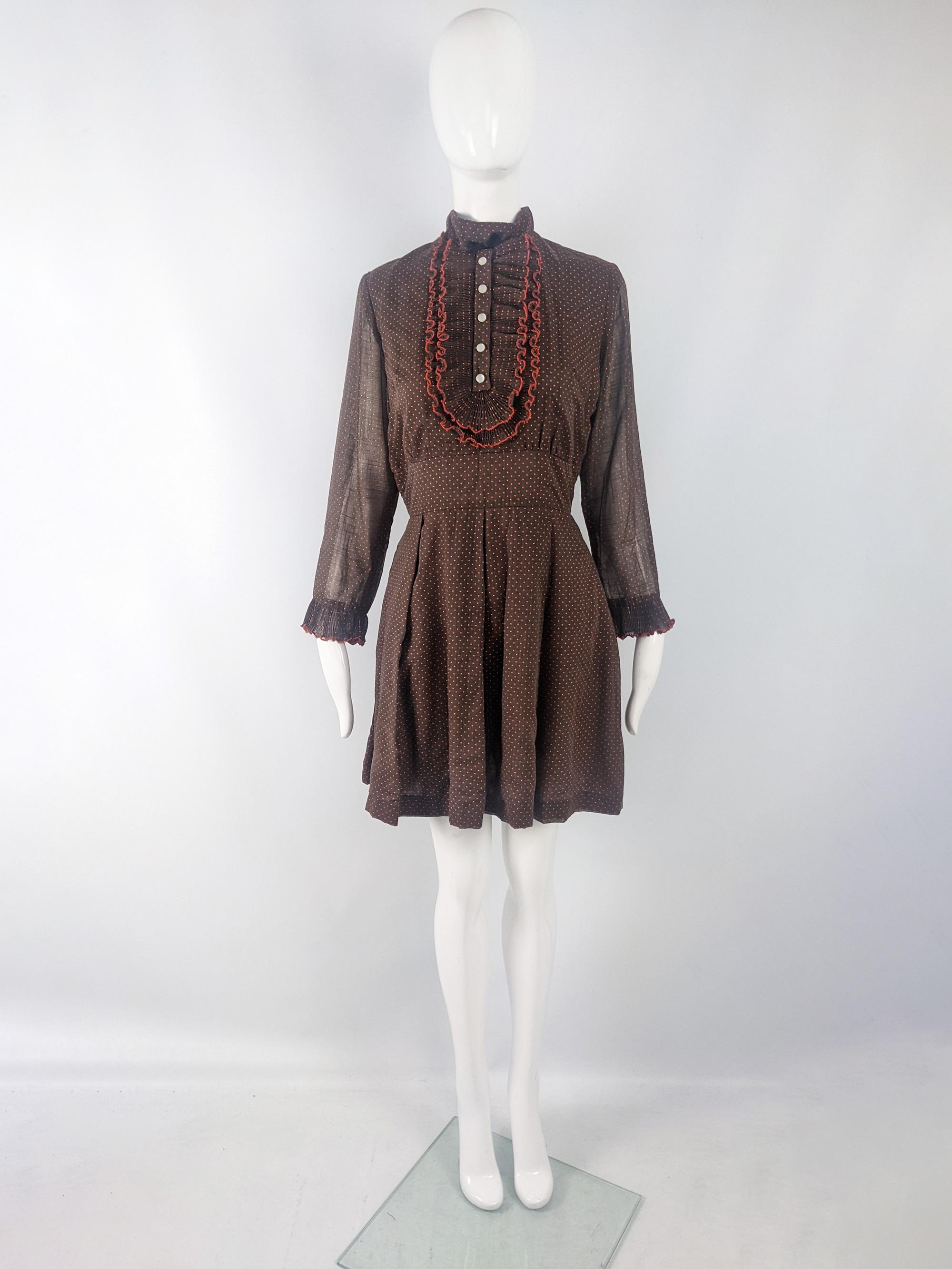 An amazing vintage womens mini dress from the late 60s / early 70s by London Deb. In a brown cotton fabric with an orange polka dot pattern throughout. It has long, sheer sleeves with a frilled cuff, a high neck and a pleated double bib collar -