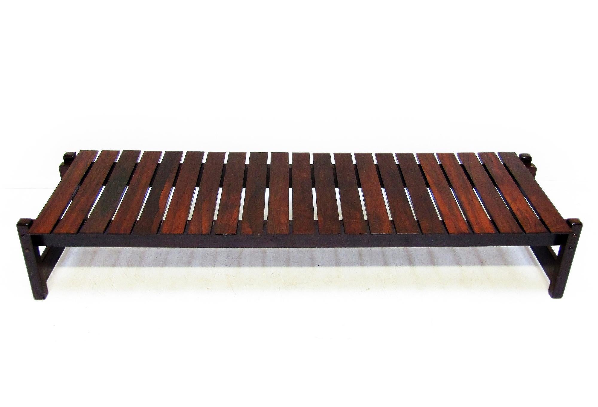 Longue et imposante table basse ou banc à lattes des années 1960 en palissandre massif de Rio. 

D'origine brésilienne, ce banc présente de nombreuses similitudes avec les designs de Sergio Rodrigues, notamment en ce qui concerne la construction du
