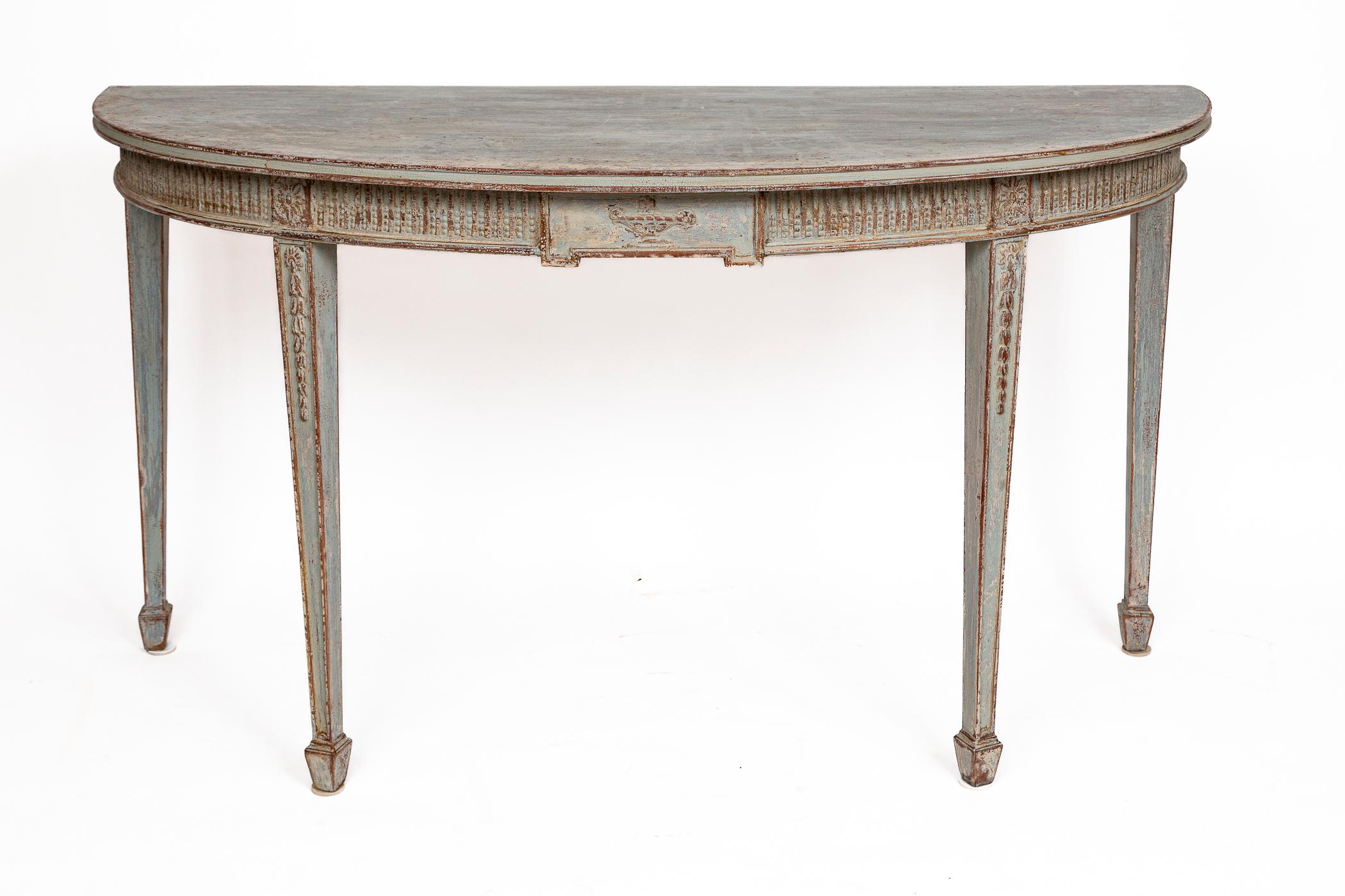 A rare longer sized Louis XVI style demilune shaped console table shown with carved neoclassic details; a delicate repetitive beaded motif along its apron with a center urn and naturalistic swags descending along its straight and tapered legs.