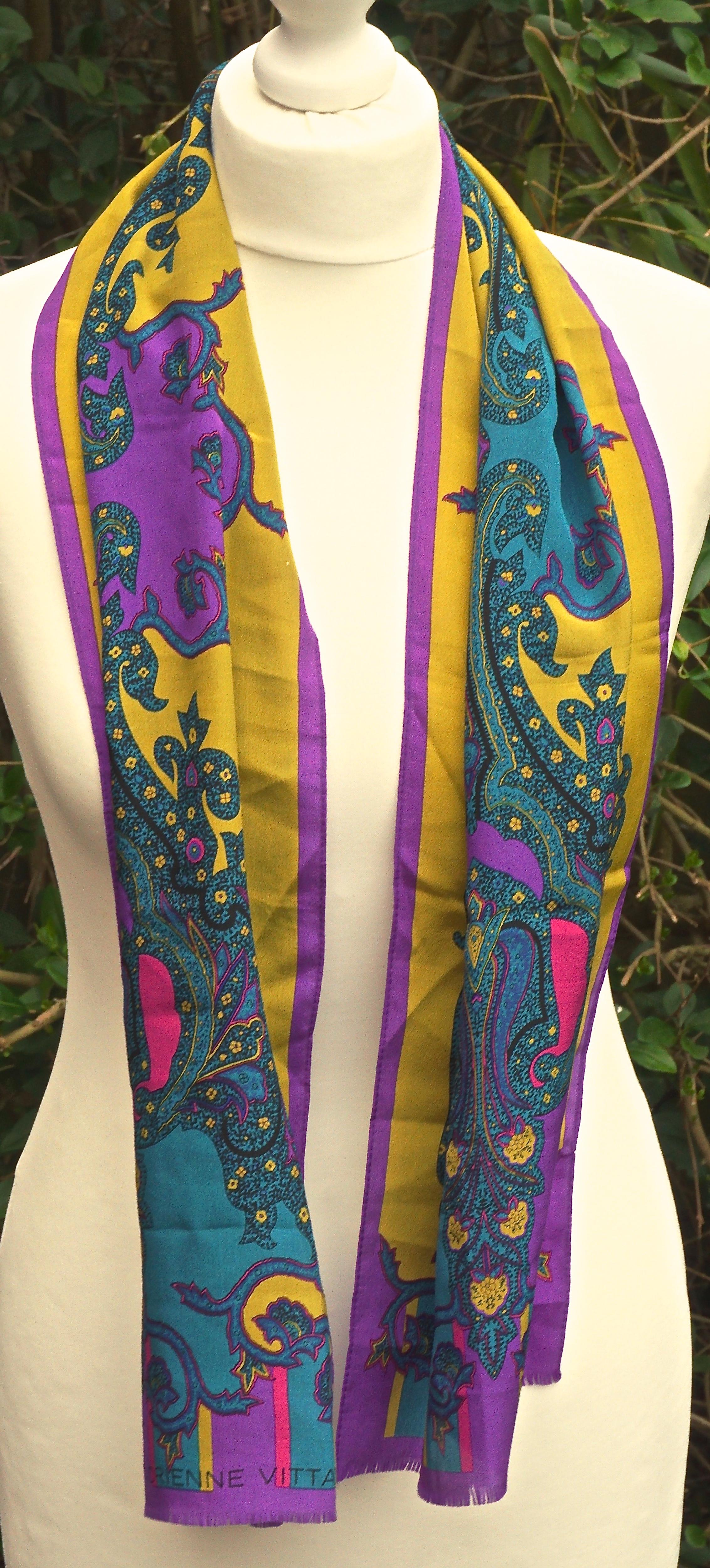 Long  Adrienne Vittadini pure silk scarf featuring a paisley print in vibrant colours of teal, pink and purple on a mustard yellow background. It has a short fringe on both ends. There are very few marks, unfortunately the scarf has recently faded