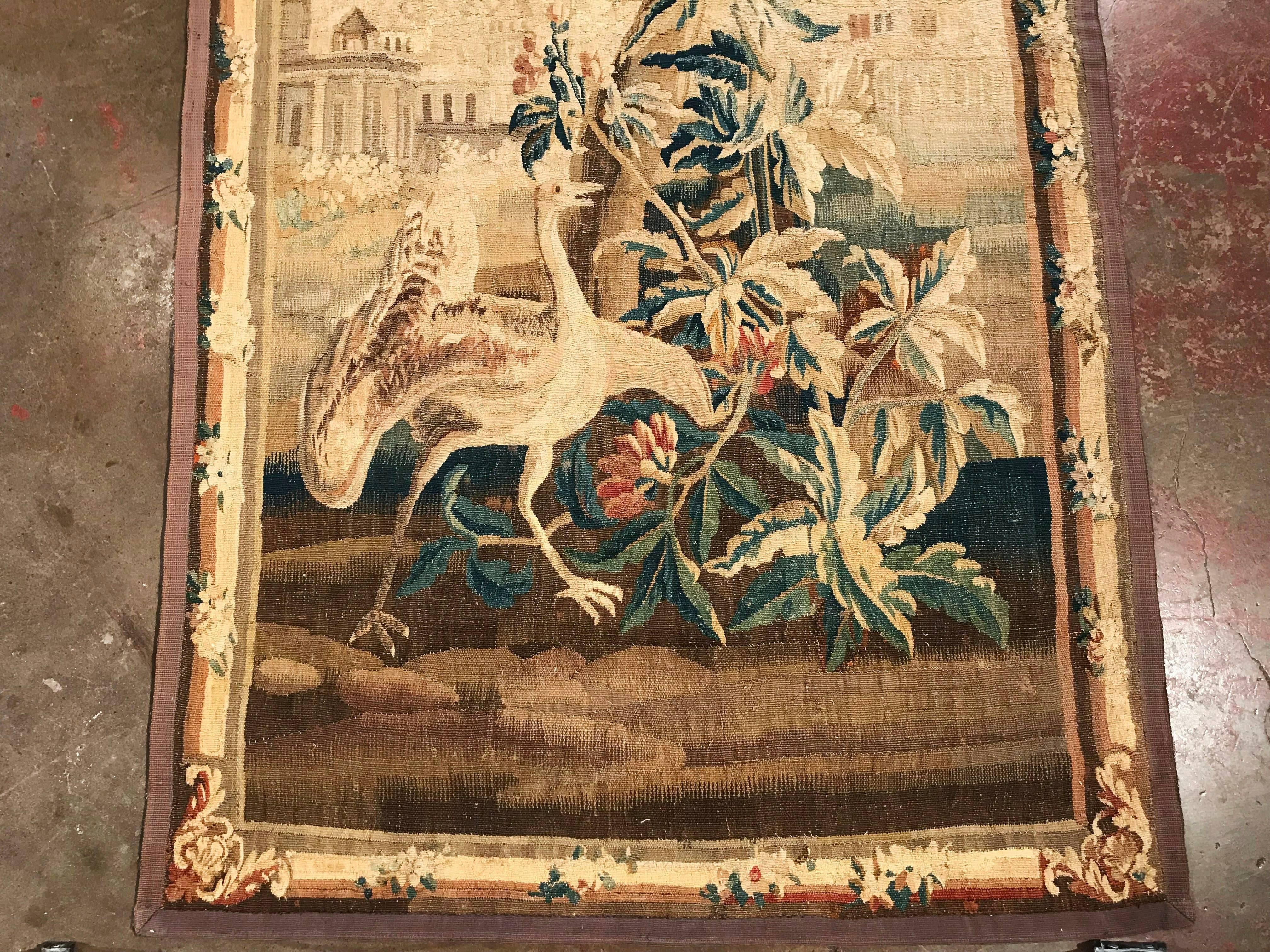 Hang this colorful, antique tapestry in your staircase or between a pair of windows. Hand woven in Aubusson, France, circa 1760, the tall and narrow wall hanging tapestry has its original floral border and illustrates a scene that includes a large