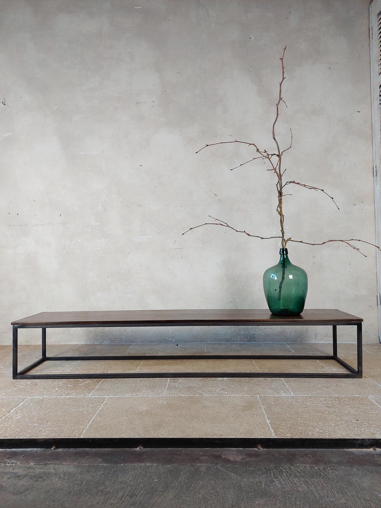 Long and narrow coffee table made of a large piece of antique walnut wood with a nice brown waxed finish. The table has a modern base made of a black steel frame. This table can be seen in the well-known Axel Vervoordt style interiors. 

 