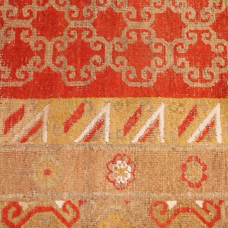 Long and narrow sunny red antique Khotan rug, country of origin: East Turkestan, date circa late 19th century. Size: 7 ft 2 in x 14 ft 2 in (2.18 m x 4.32 m)

 Khotan rugs are unique in their presentation, utilizing vast expanses of negative space