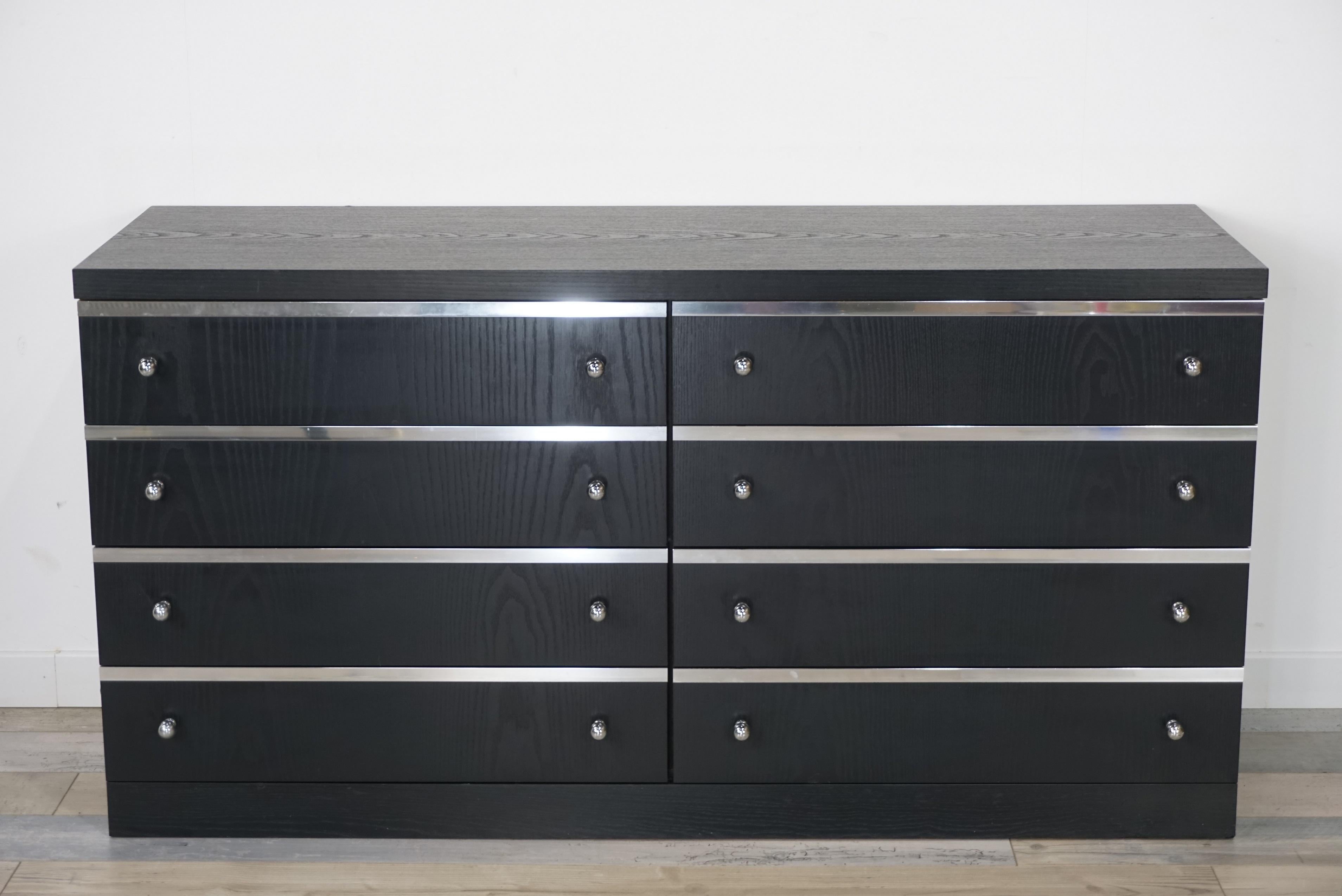 Long black wooden and chrome vintage chest of drawers with sober lines and Minimalist design offering large storage spaces: eight drawers that have for each their facade decorated with a chrome edging and chrome metal handle, too.
In very good