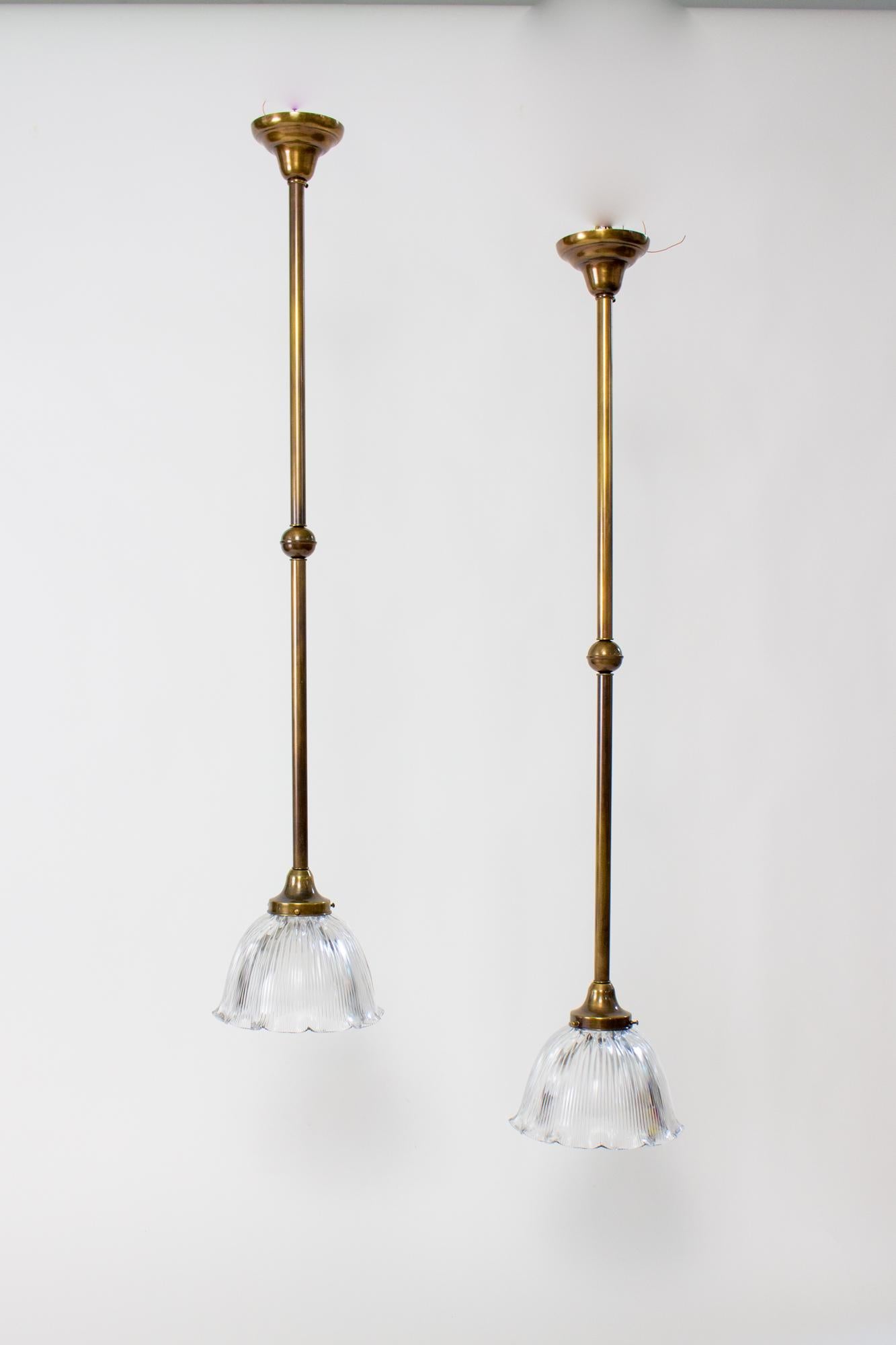 Long antique brass pendant with prismatic glass, a pair, 49” long. This pair of traditional pole pedants are made from a solid brass with an antique patina. They have a bell shaped canopy, long tube, with a spherical break in the middle, and a