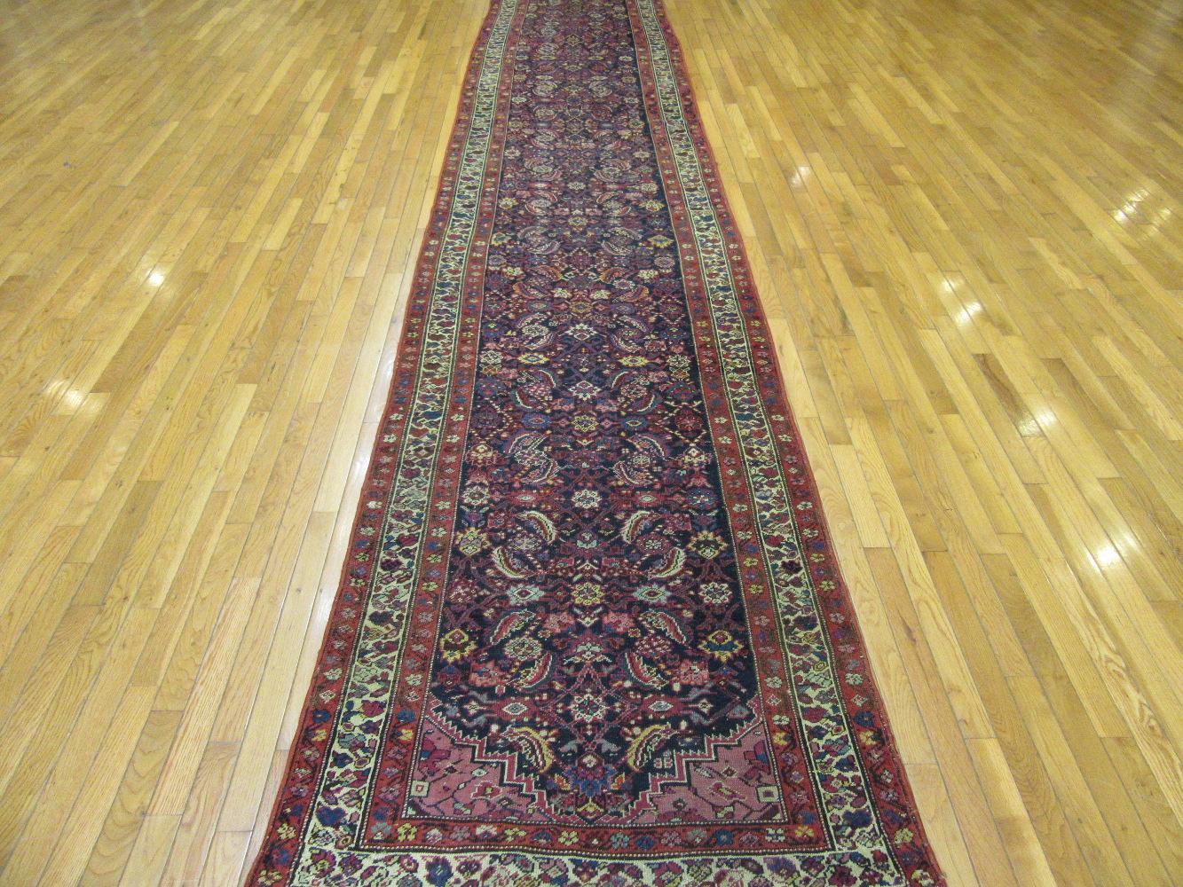 This is a long hand knotted antique Persian Malayer runner rug. It is made with Persian wool colored with natural dyes on a cotton foundation. It has a small scale Herati pattern on a navy blue color background. It would enhance the look of any hall