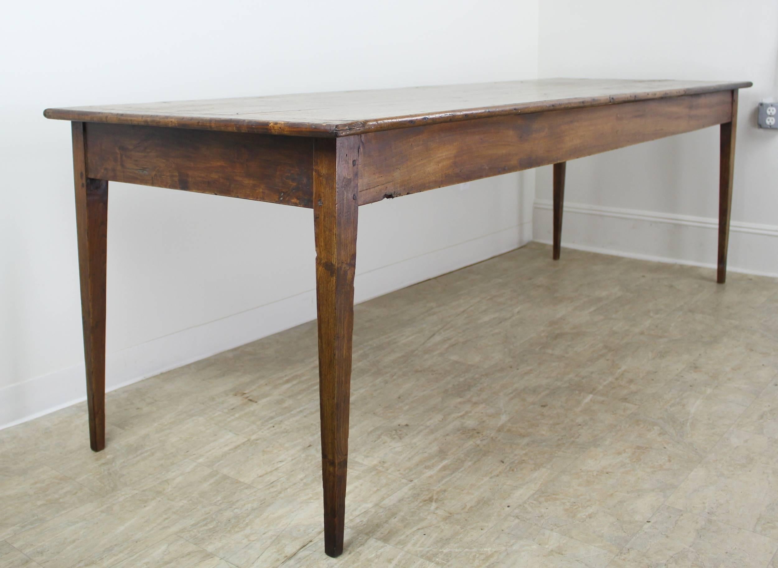 A long beautifully grained and colored antique poplar farm table from France. Rich patina and natural grain and knotholes elevate this country piece of furniture to art! Thin tapered legs and a high apron height of 25 inches creates a particularly