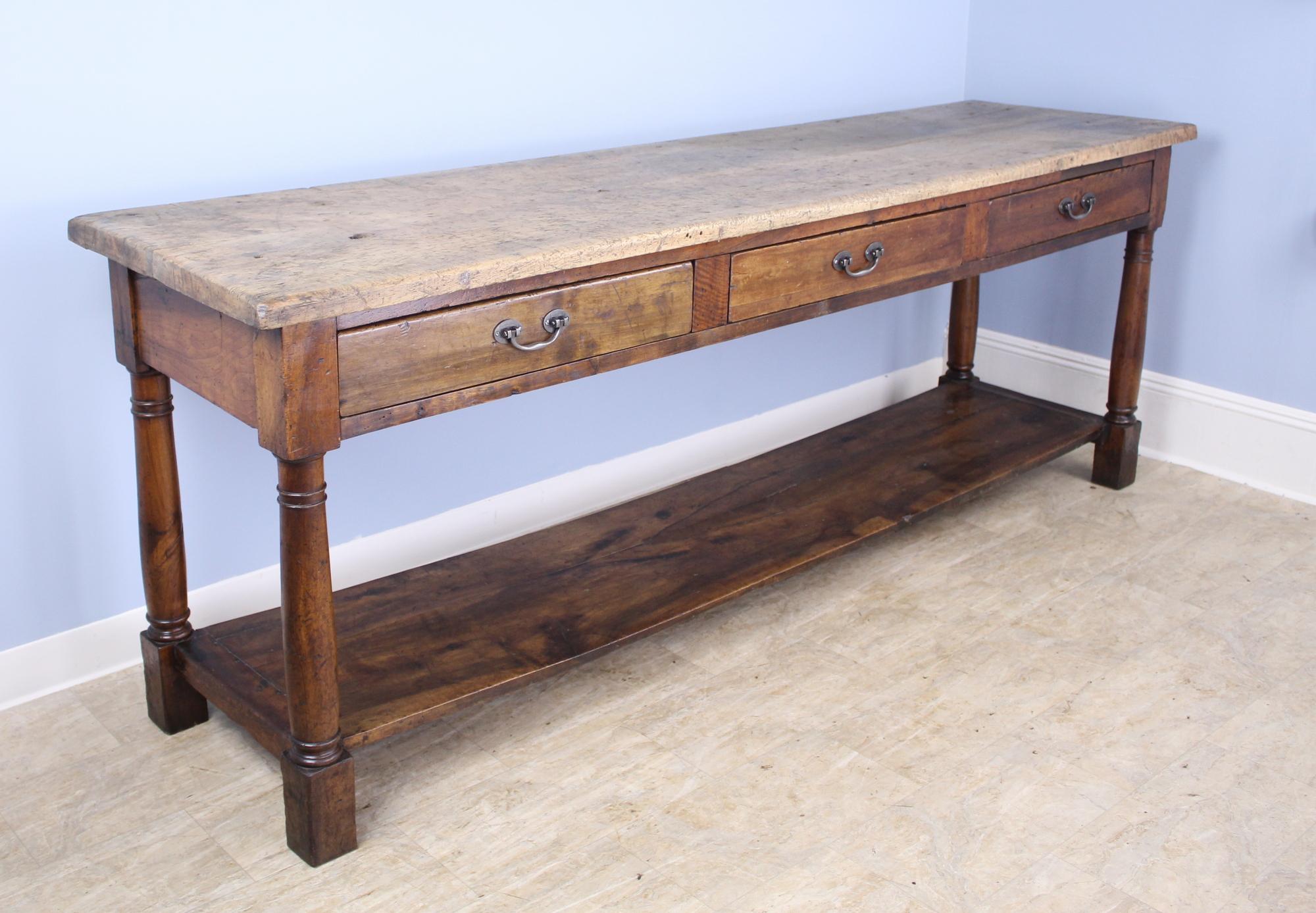 A very long, fabulous English draper's table, originally for use by a tailor or seamstress. The top is quite distressed and scrubbed; evidence of its long industrial use. The polished walnut base has lovely color, grain, and patina. Three roomy