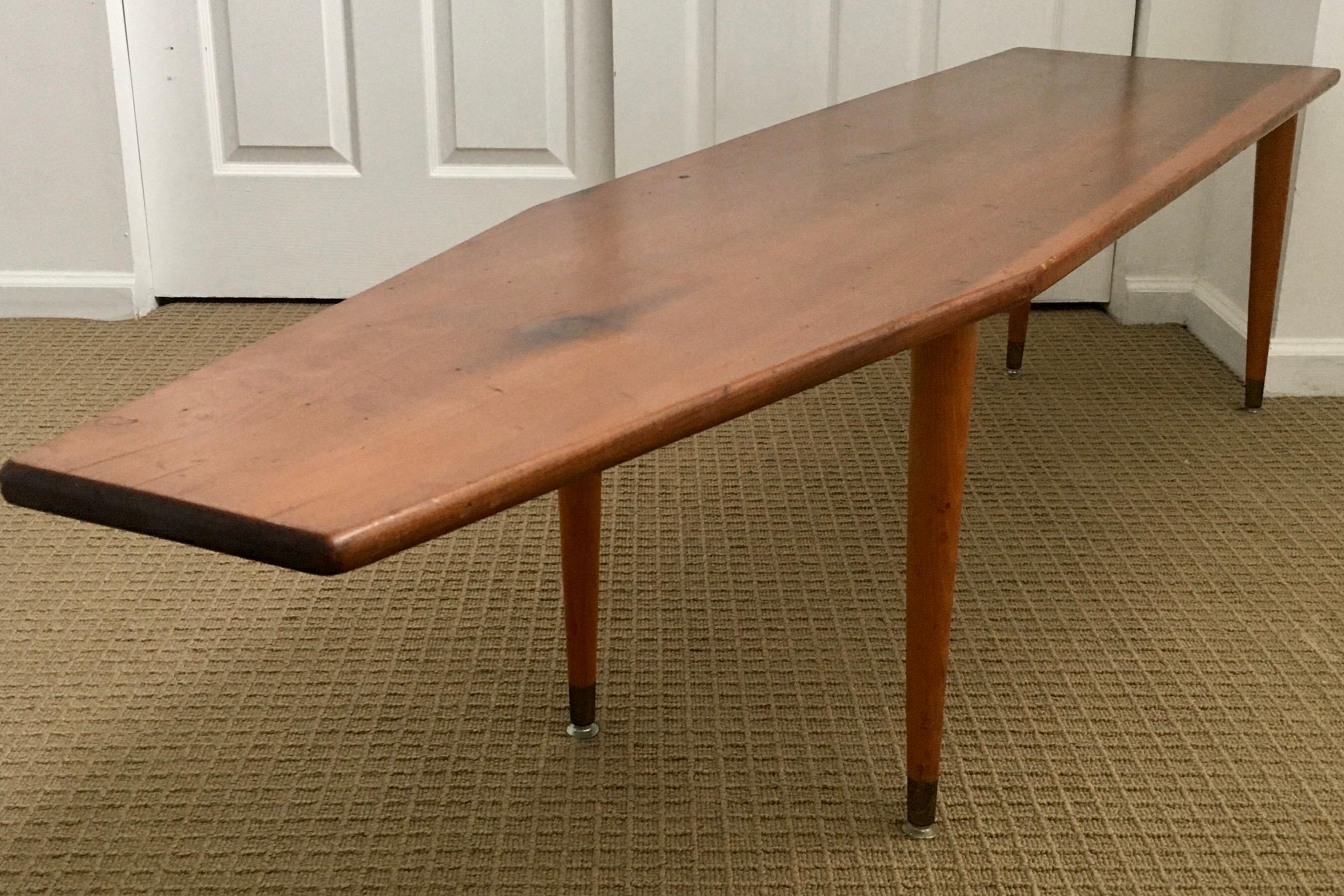 Long Mid-Century Modern asymmetrical surfboard shaped wood coffee table. This Danish style cocktail table features a sculptural top suspended on four tapered legs.
         