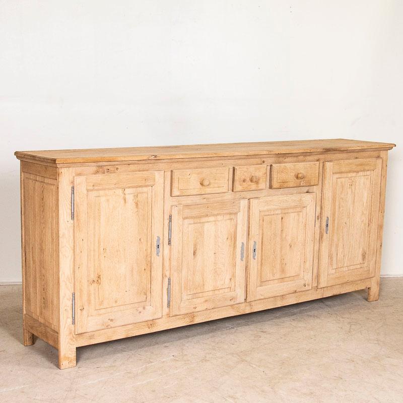 This vintage long oak sideboard has been bleached giving it a fresh and welcoming look for today's modern home. The three drawers have wood pulls and balance over two panel doors. At almost 8' long, it will serve well as a buffet, sideboard or
