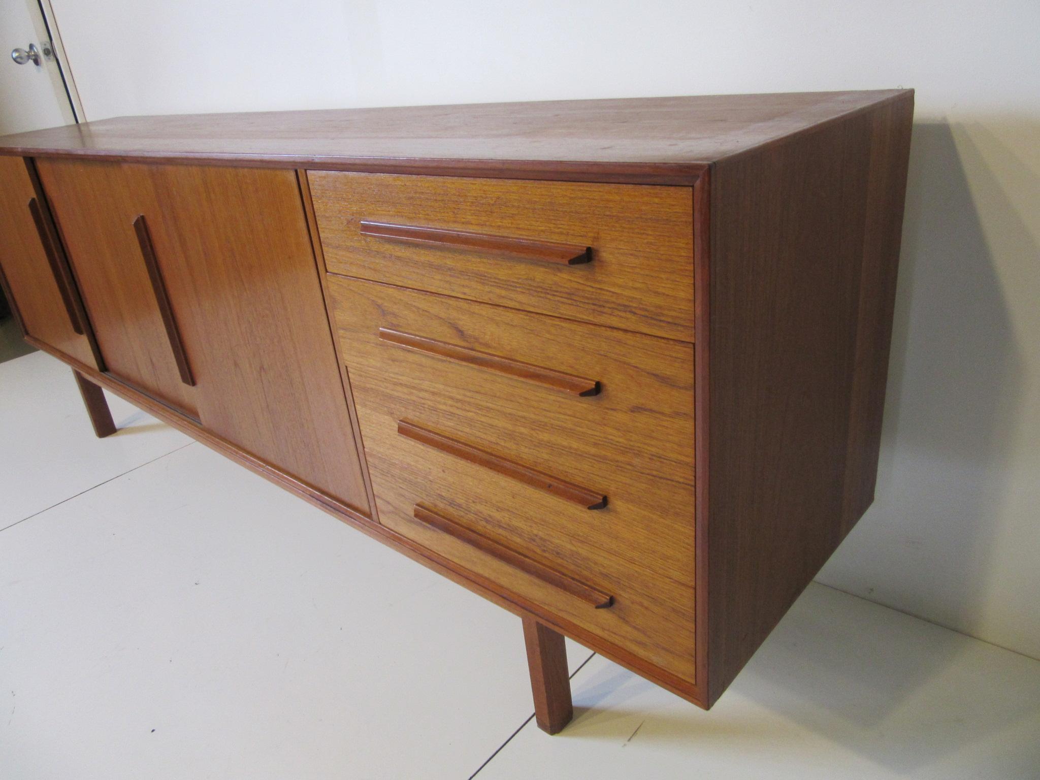A longer Danish teak wood credenza or server with four drawers, three sliding doors which one contains two small drawers and the other two areas have nonadjustable shelves. Very well crafted with ample storage designed in the manner of IB