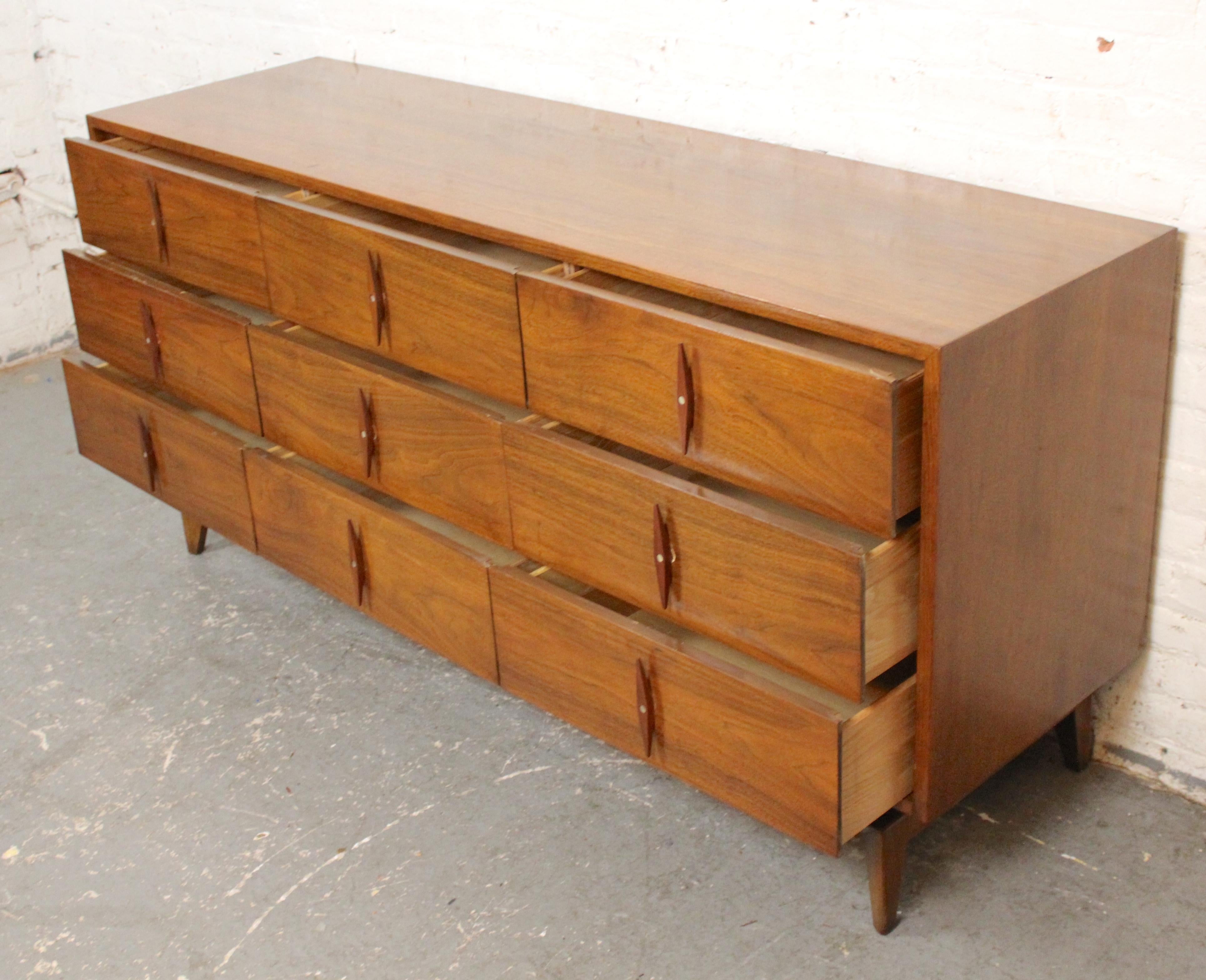 Long mid-century modern dresser by American of Martinsville, designed with pointed diamond handles on each of the nine drawers. Warm walnut grain throughout the piece with tapered legs.
Please confirm location NY or NJ