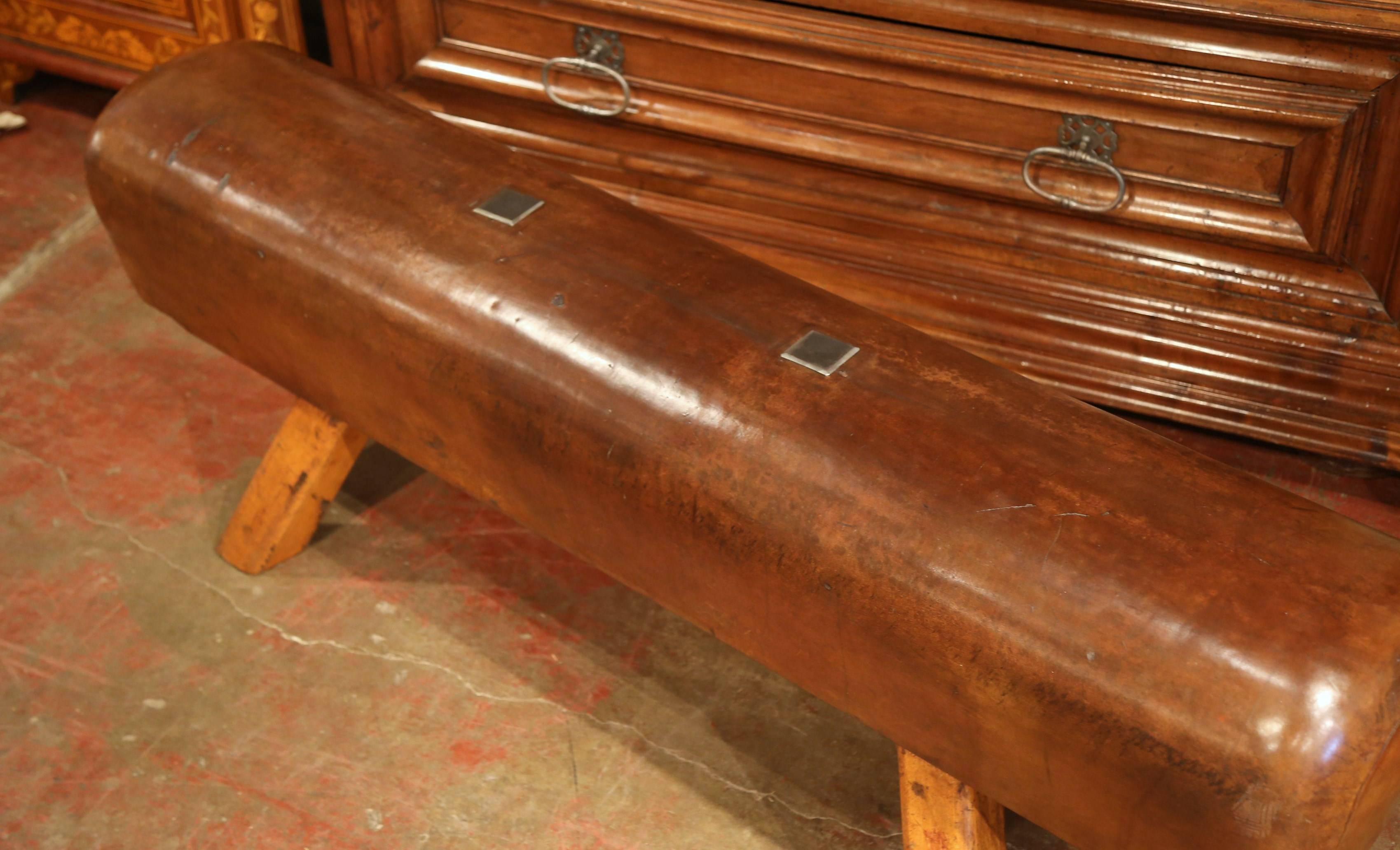 This antique, leather pommel horse bench was crafted in the Czech Republic, circa 1920. The rustic piece features four wooden legs, original leather and custom steel plates which have been added to cover the location of the original handles. This