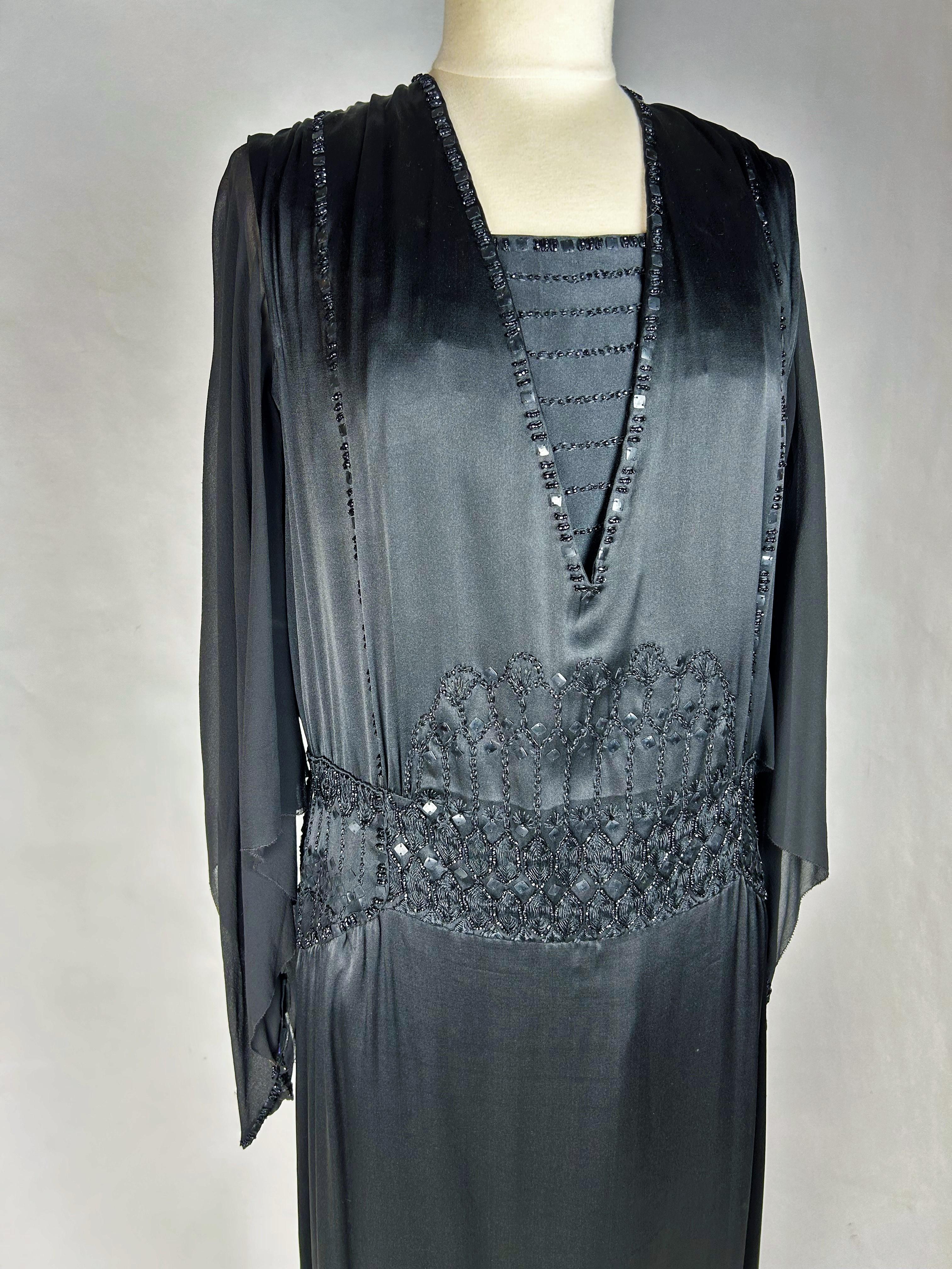 Vers 1920-1930. France Paris
Robe longue du soir en satin Duchesse et mousseline noire de Olivan-Brevet & Berthe, 14 rue de Helder, Paris, datant de la fin des années 1920. Robe ample au large décolleté en V ponctué d'un détail de pudeur, fermée
