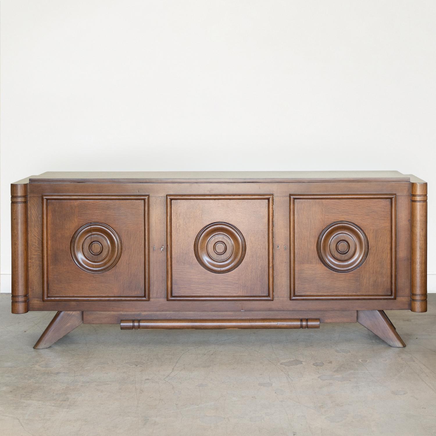 Incredible long wood sideboard by Charles Dudouyt from France, 1940's. Beautiful carved wood circles on cabinet doors and carved tapered legs. Three sections each with a middle shelf and center section with top drawer for added storage. Newly