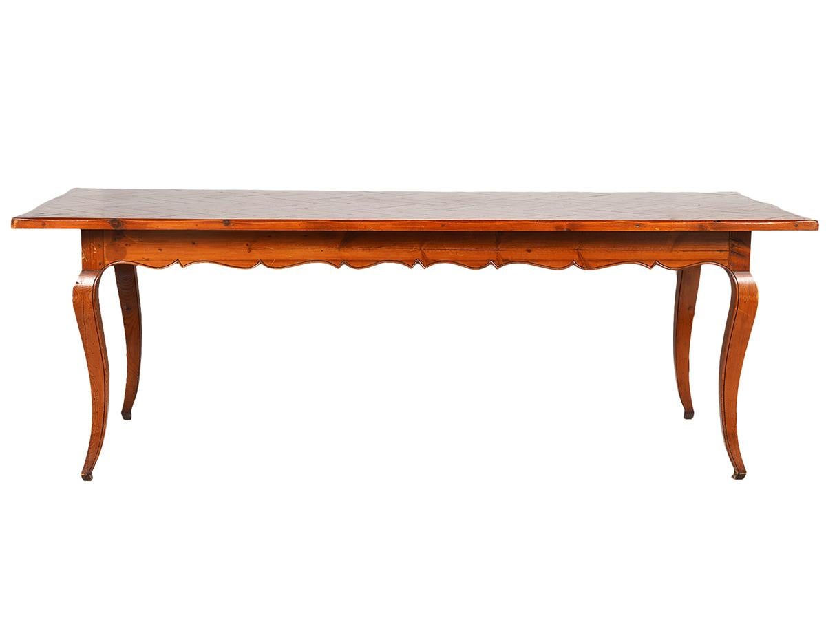 Of a glowing warm aged pine color this long French provincial style dining table features a beautiful pine parquetry top above a frame with carved scalloped apron resting on four carved cabriole legs.
