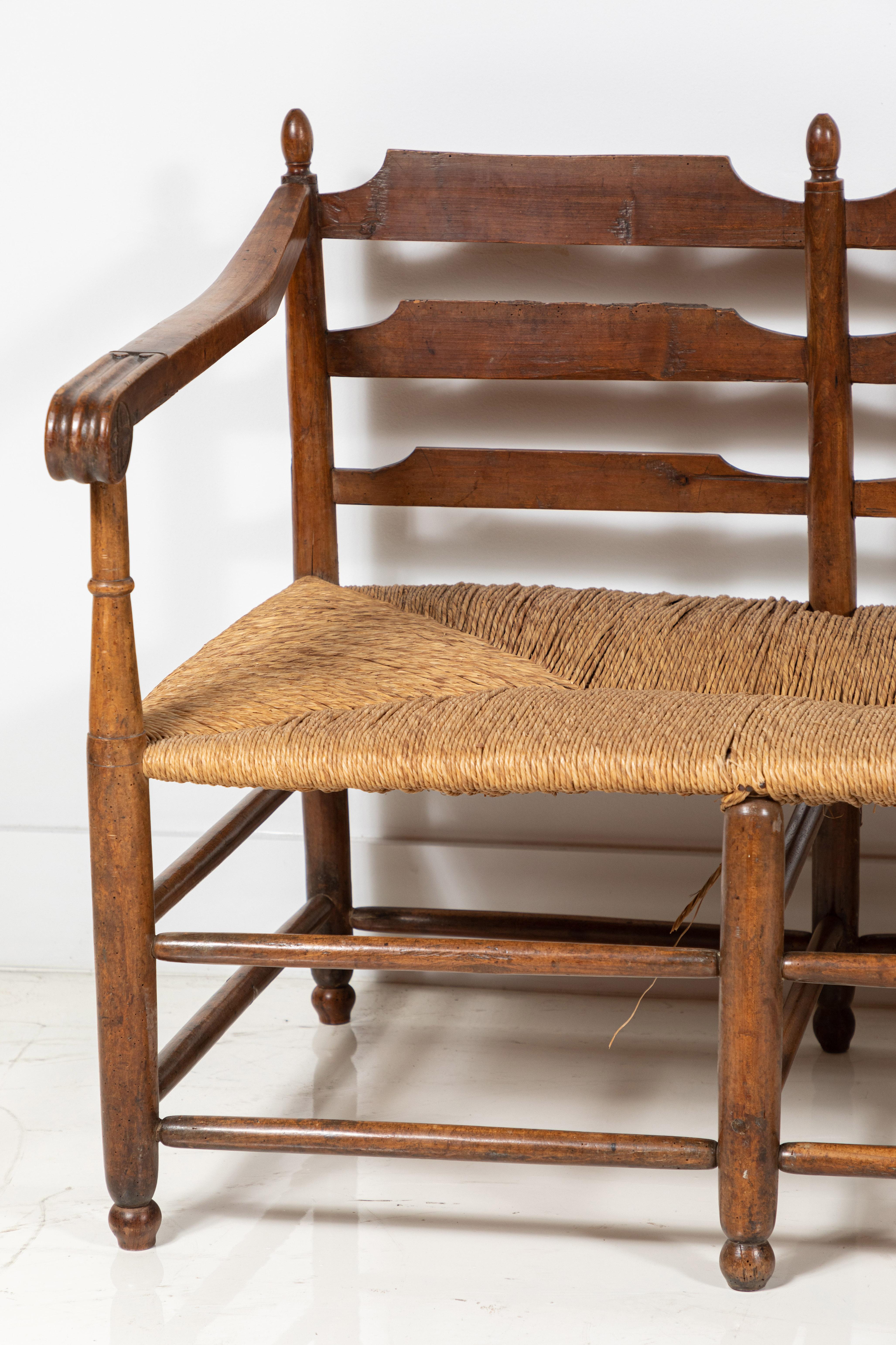 Long French bench with scrolled arms and wooden ladder back details. Original rush is in great condition.