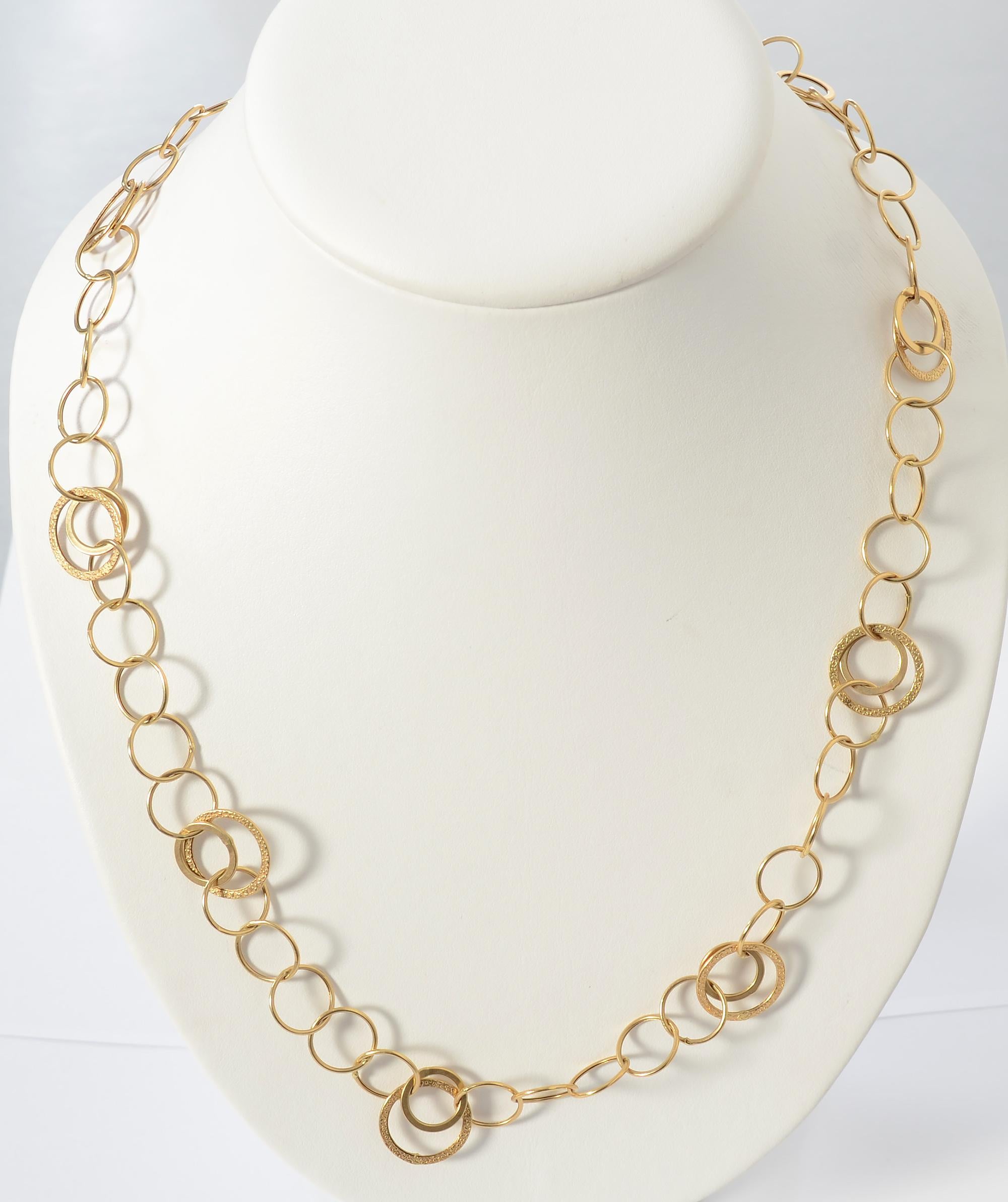 Merveilleusement sportif, ce long collier à chaîne en or est composé de trois cercles de tailles différentes. Deux des tailles ont une finition brillante et la plus grande a une texture en relief. Les plus grands cercles ont un diamètre de 5/8