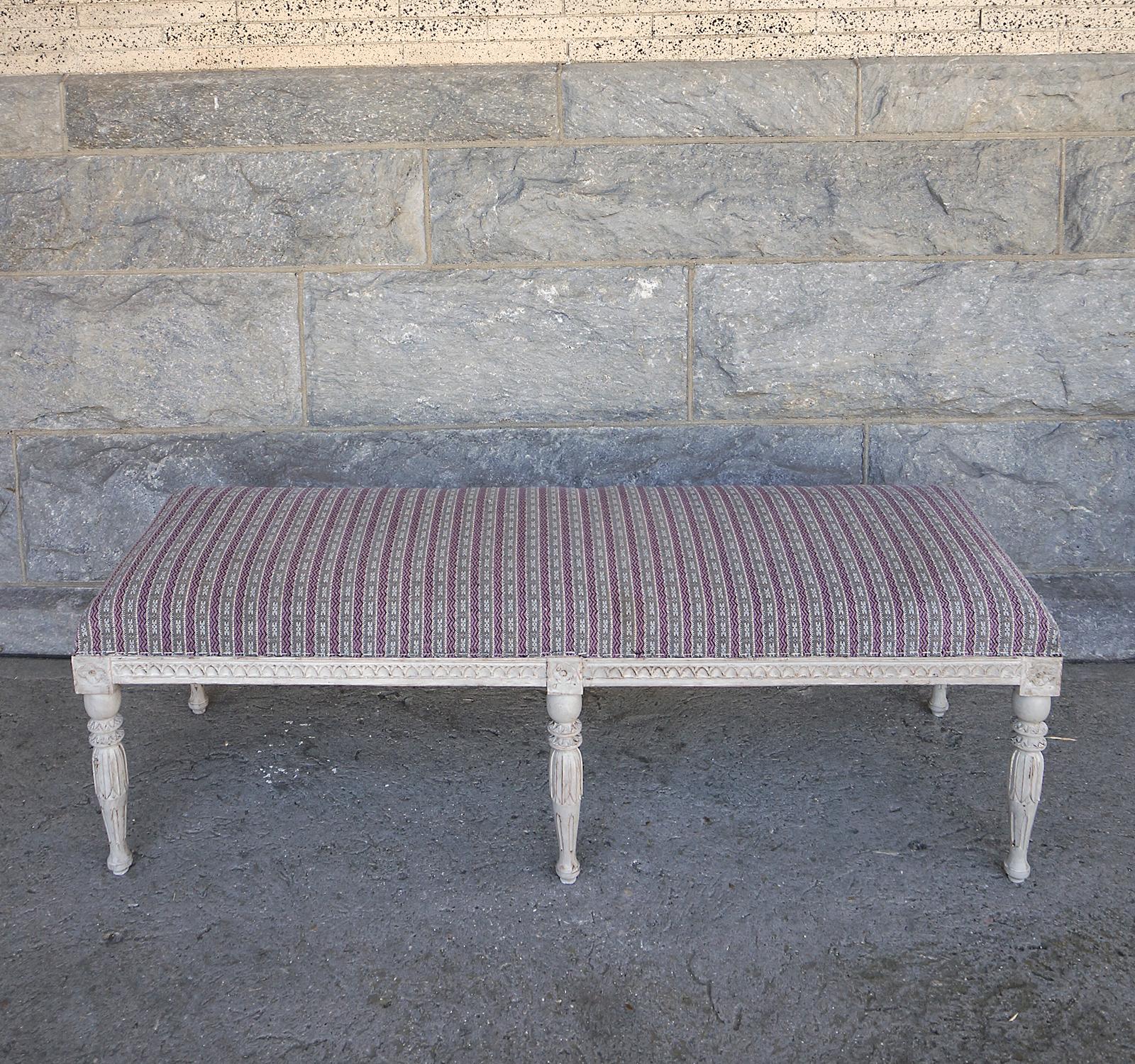 Upholstered Swedish bench, circa 1880, in the Gustavian style. Nicely carved lamb’s tongue molding along the seat rails, interrupted by blocks with carved rosettes where each of the six legs is attached. Sturdy and comfortable, and ready for your