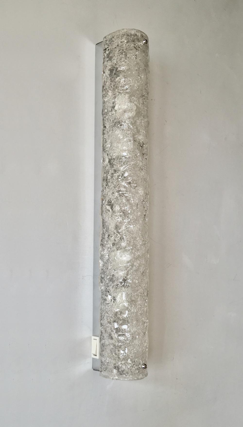 Long, slim ice glass sconce by Hillebrand, Germany, 1960s. 

Curved glass shade of bubbled and textured glass over a silver-coloured chrome back plate. White switch to one side. In the main image, natural light is coming through the glass.

The