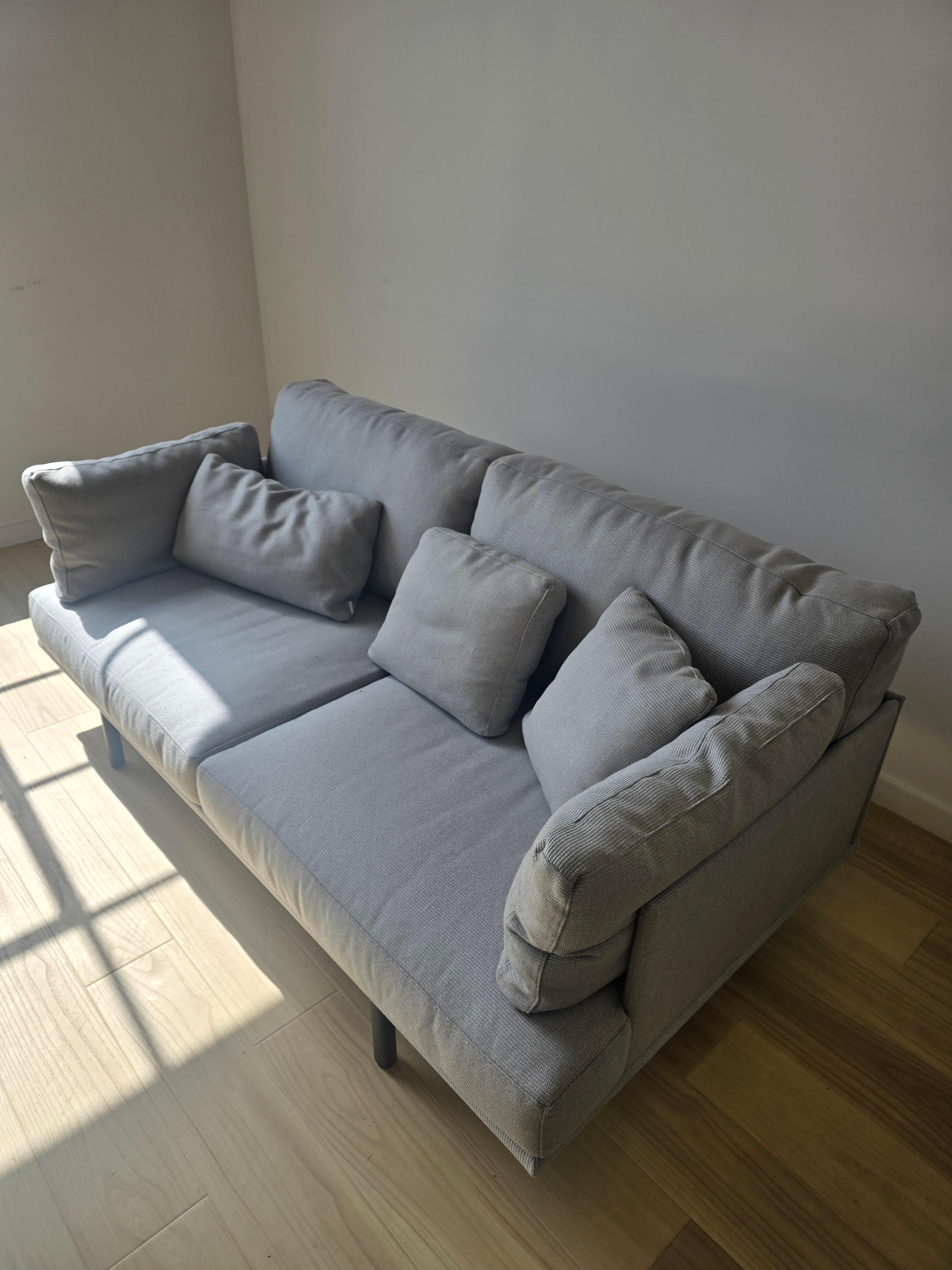 Sofá 2 con armazón de aluminio con recubrimiento en polvo y patas regulables. Acabado de aluminio en color: Gris metalizado 56 y Blanco mineral 34. Cojín de asiento y respaldo de espuma de poliuretano de alta resistencia de 35 kg. Los cojines del