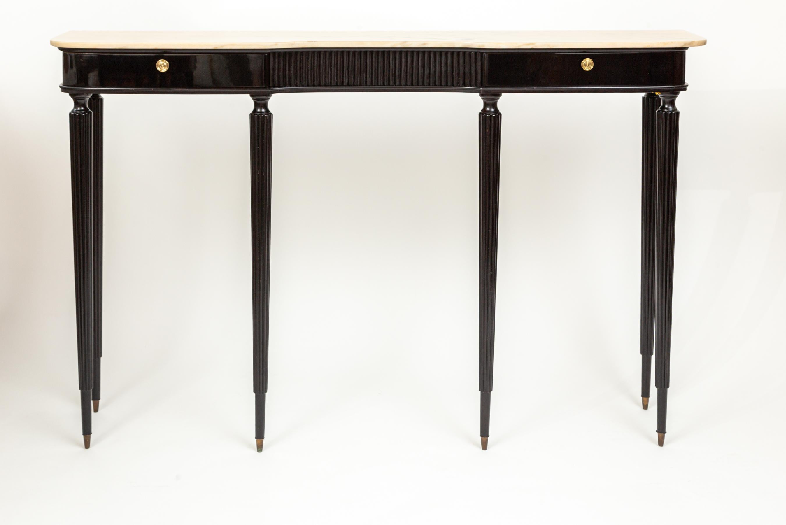 A  very long and narrow modified neoclassical style console with a warm crème marble top above a black lacquered on beech frame consisting of two drawers set into a concaved apron with reeded center panel and finishing on six tall rounded and reeded