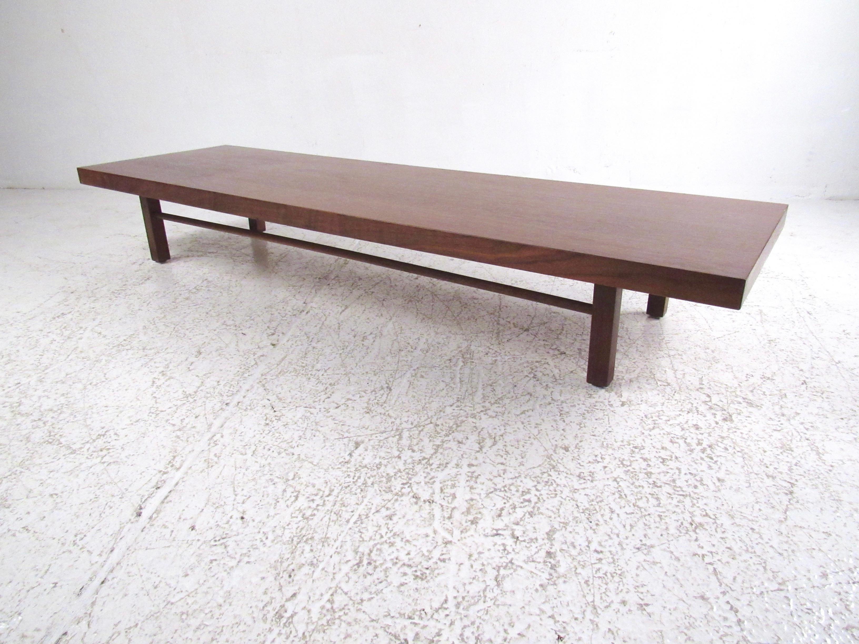 This stylish midcentury cocktail table features a vintage walnut finish with striking modern lines and tapered wooden stretchers. Designed by Milo Baughman for Thayer Coggin the sleek vintage modern design of this long low coffee table makes the