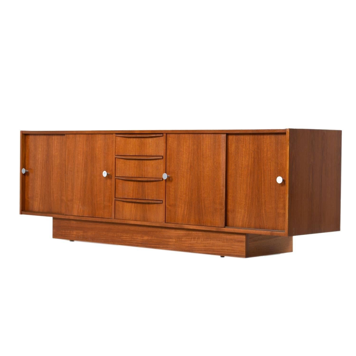 Expertly crafted vintage Danish teak credenza. The unit features convenient sliding doors that conceal cabinet space at left and right. An uncommon mix of drawers and cabinet space make this piece versatile. Use it as a dresser in the bedroom, TV